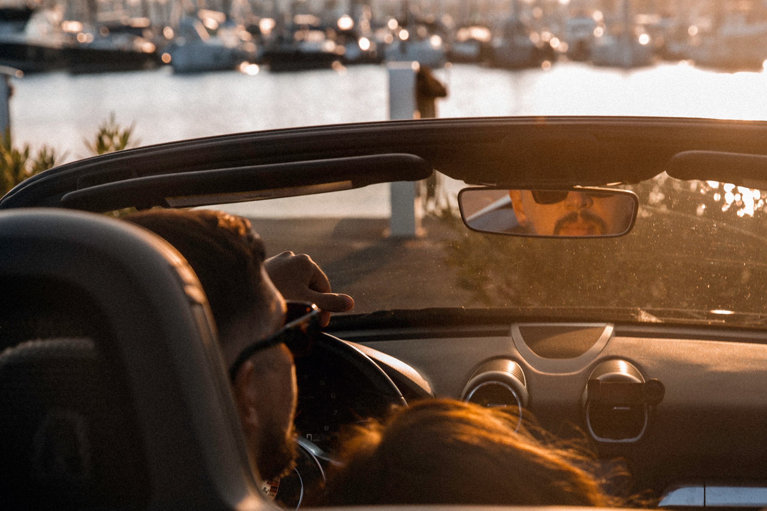 Sesión de fotos love story de pareja en València, España, capturando un momento íntimo de una pareja conduciendo un coche descapotable durante la golden hour, con luz cálida del atardecer, reflejos cinematográficos y una atmósfera lifestyle romántica que transmite espontaneidad y emoción — ideal para fotografía love story, sesiones de pareja, reportajes de compromiso, retratos lifestyle cinematográficos y fotografía romántica de pareja en València y en toda España.