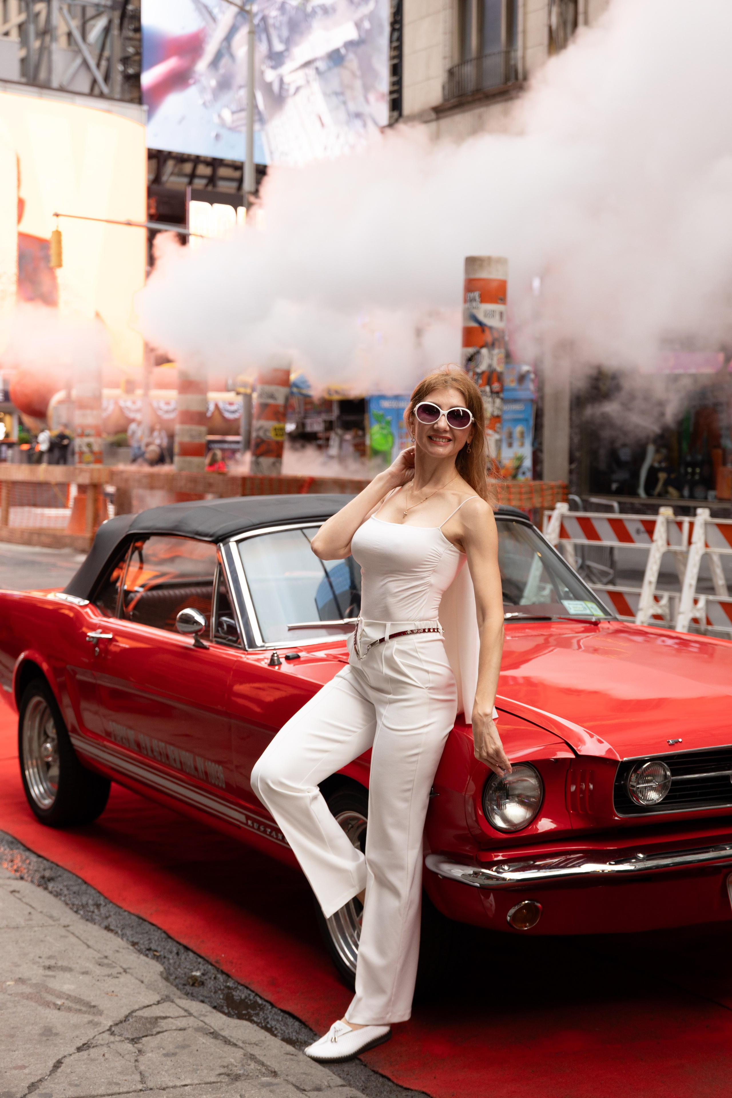 Woman posing beside a classic red Mustang in Times Square