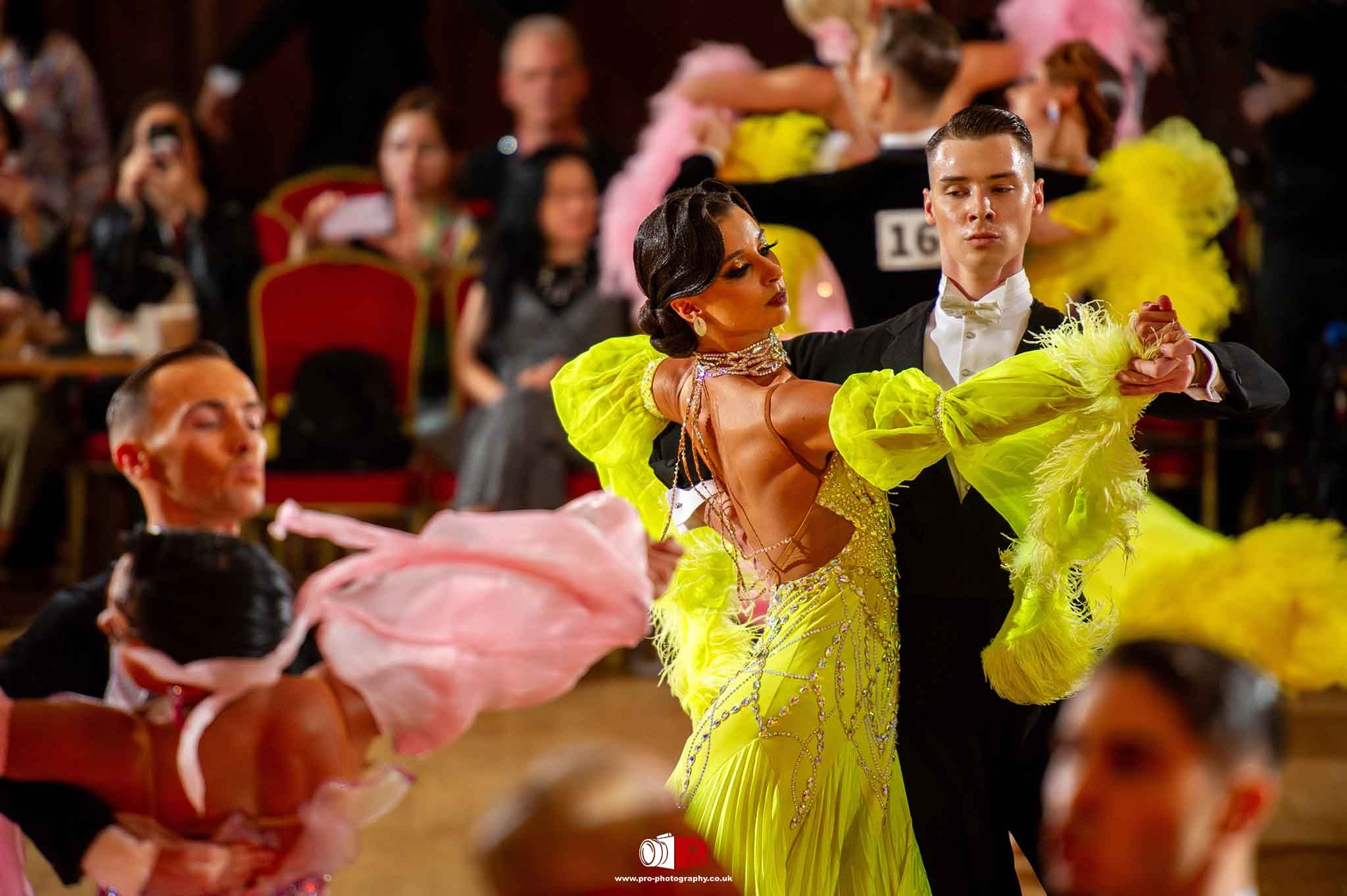 Graceful ballroom dancers in vibrant yellow and black attire perform a synchronized routine.