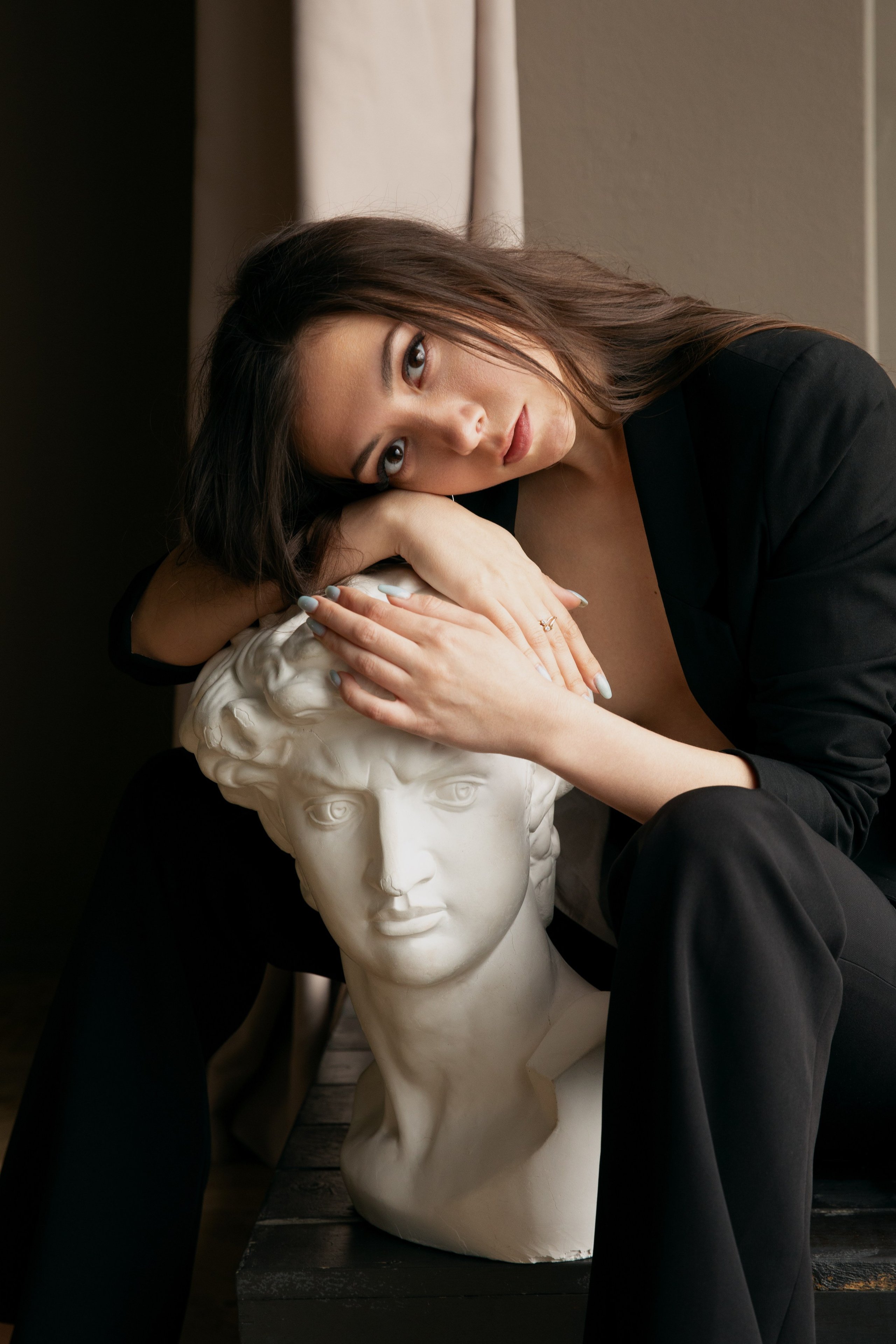 Frau lehnt Kopf auf weiße klassische Skulptur im Studio
