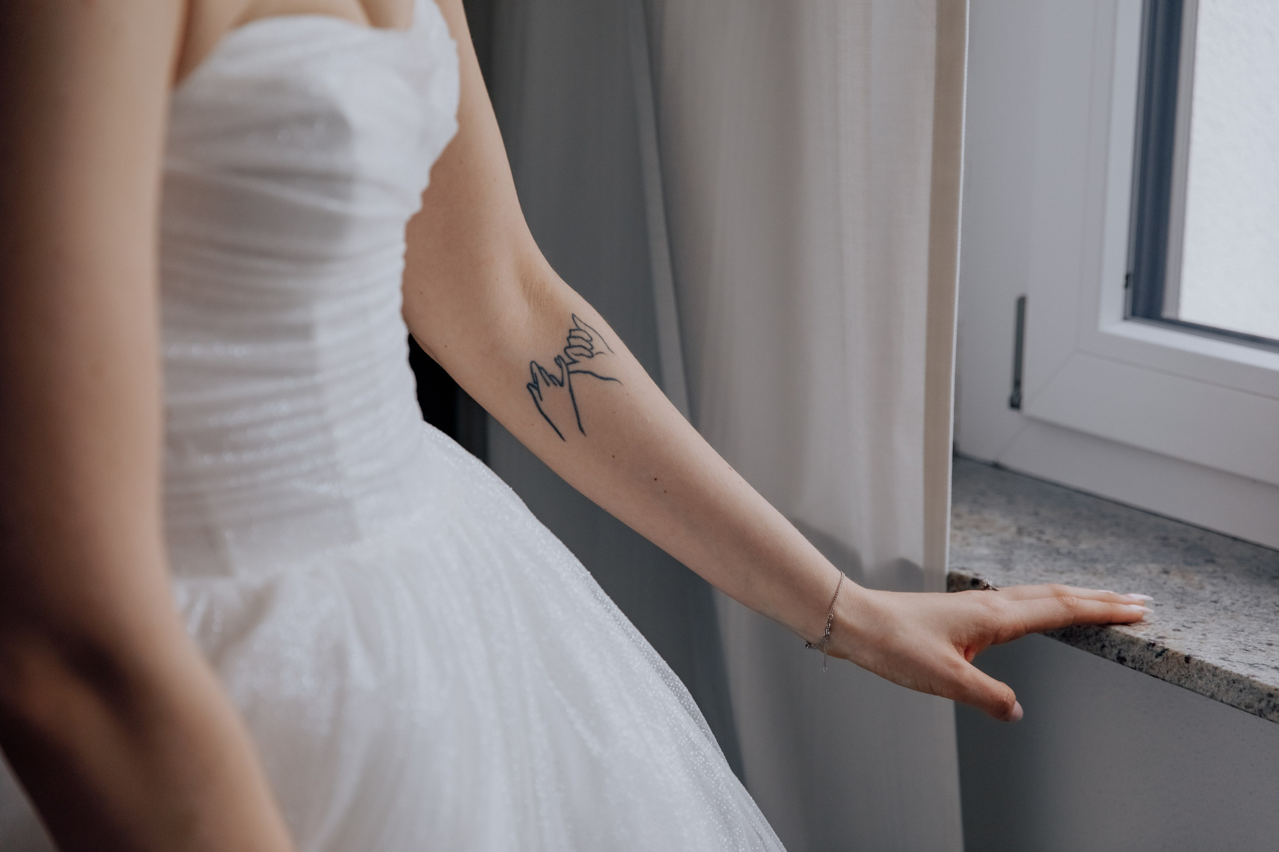 Detailaufnahme der Hand der Braut mit einem Freundschafts-Tattoo. Ein symbolischer Moment der Hochzeitsvorbereitung.