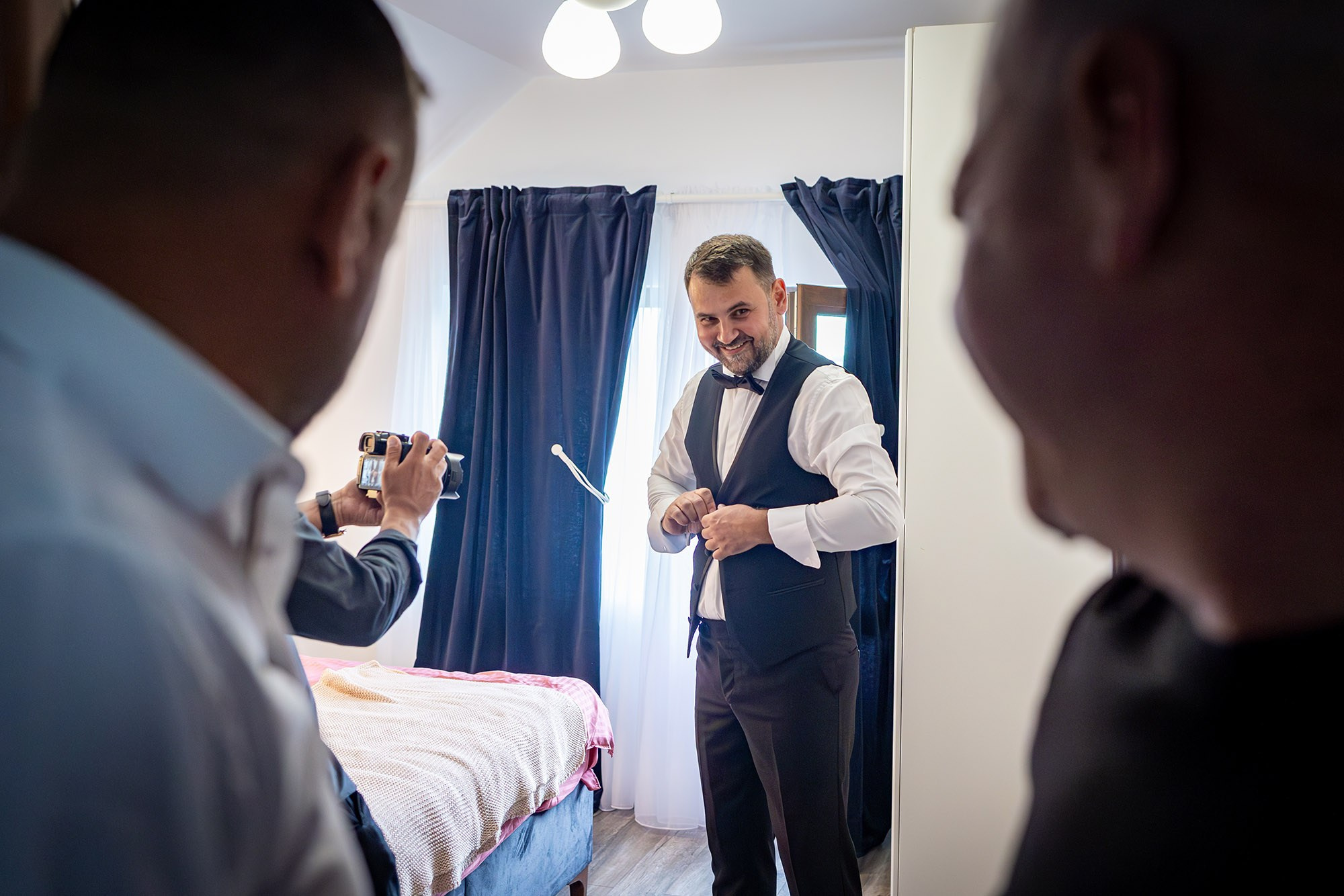 Mire zâmbitor în vestă și papion negru, filmat de un prieten în timp ce se îmbracă pentru nuntă