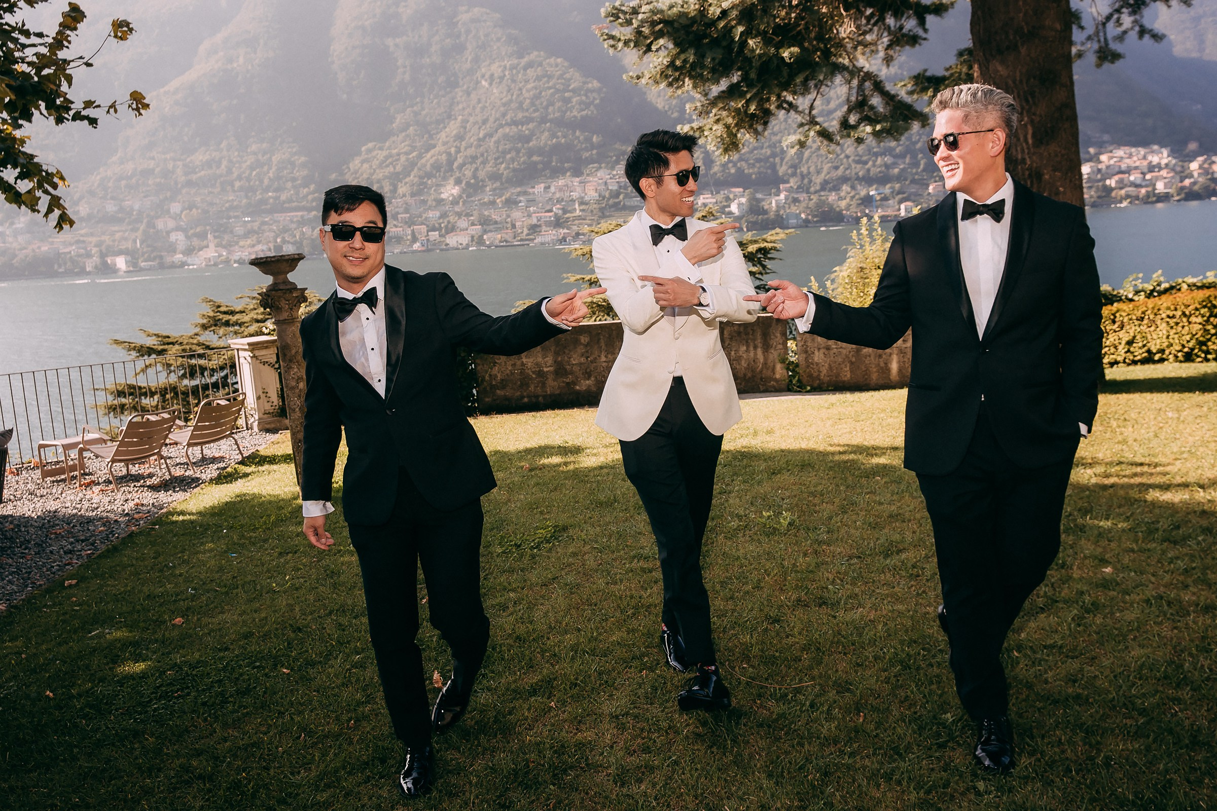 Groom and groomsmen walk across a lawn, playfully gesturing at each other near Lake Como in Villa Lario. 