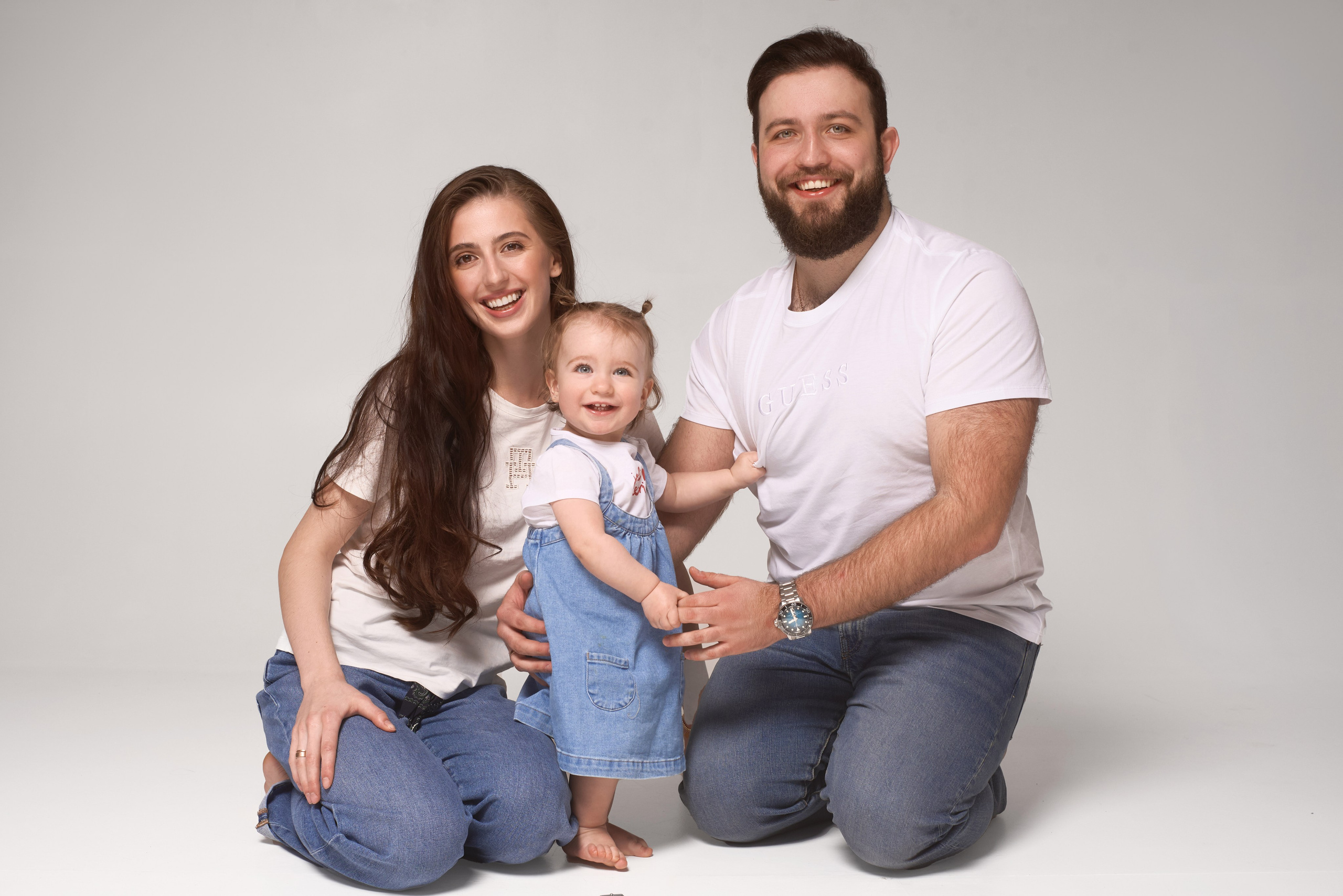 Profesjonalna fotografia rodzinna – rodzice z córką w jasnych, casualowych stylizacjach na neutralnym tle