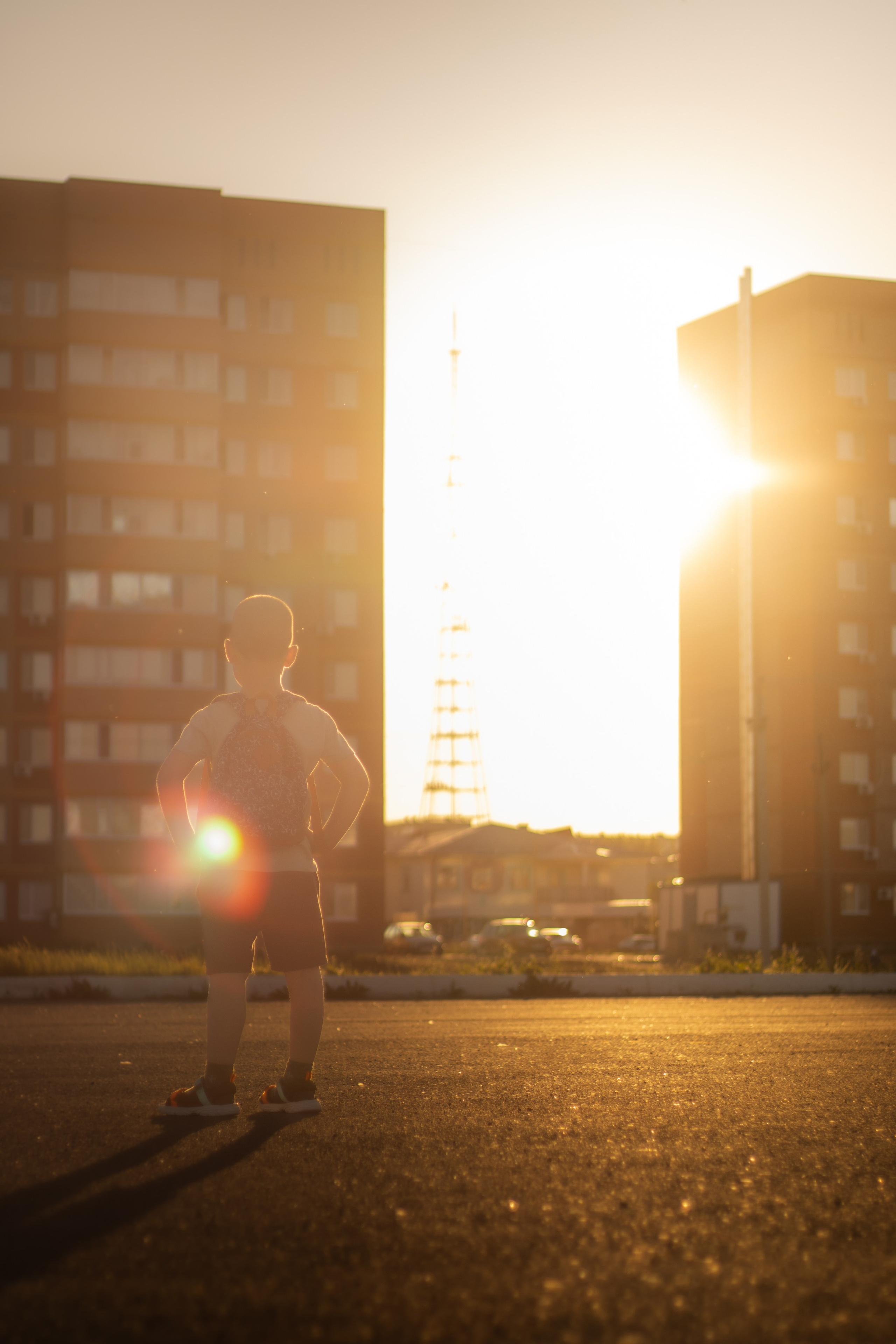 Atmosférická městská krajina s dítětem při západu slunce s výrazným světelným odleskem.