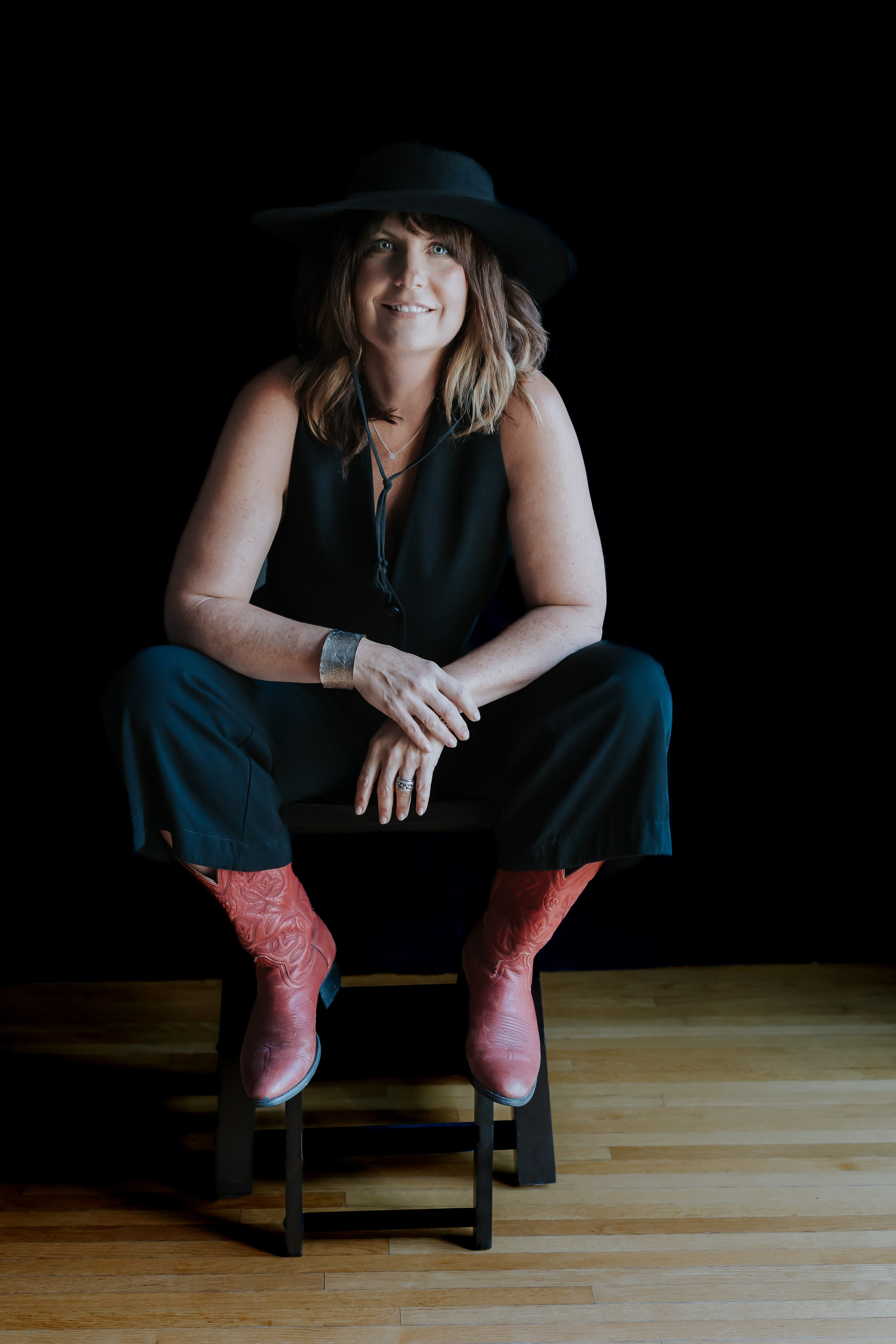 woman in red cowboy boots on black backdrop staring at camera 