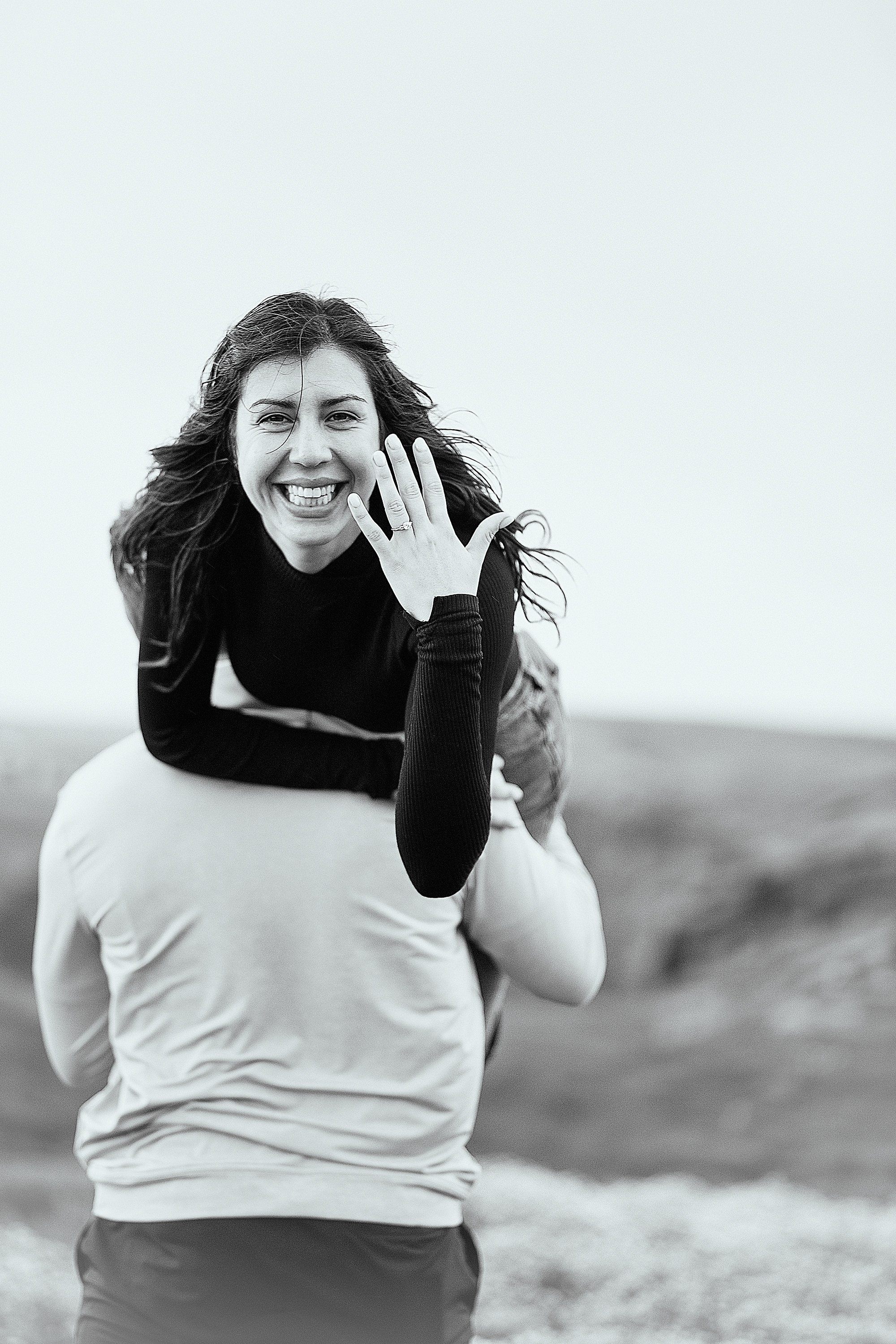 A woman laughing and excitedly showing her engagement ring, with the Irish landscape in the background.