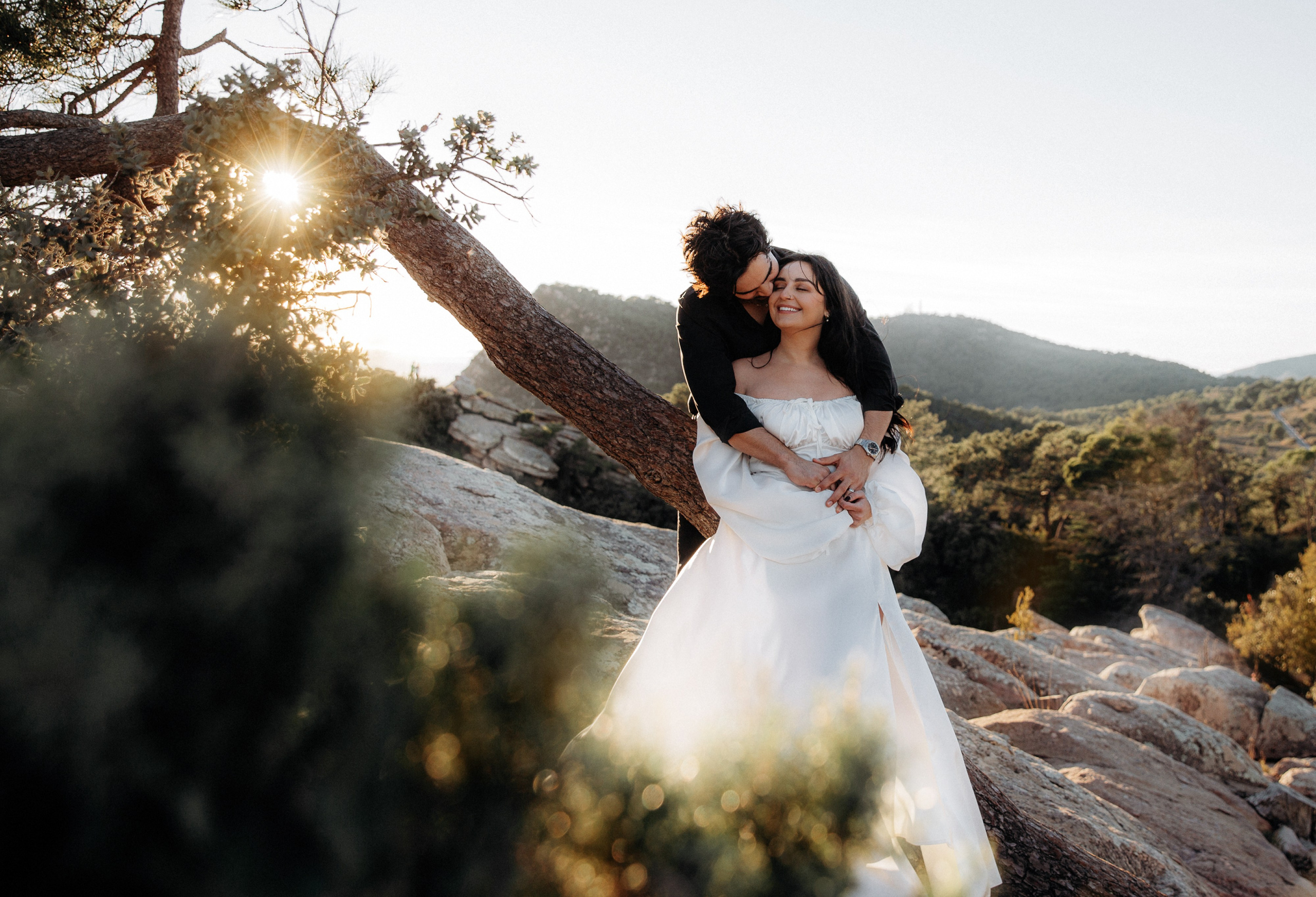 Engagement photoshoot in València, Spain, capturing a joyful, romantic moment of a couple embracing outdoors during golden hour, with soft sunlight, natural greenery, and scenic hills in the background — perfect for engagement photography, wedding love stories, romantic couple portraits, and professional engagement and wedding photoshoots in València and across Spain.