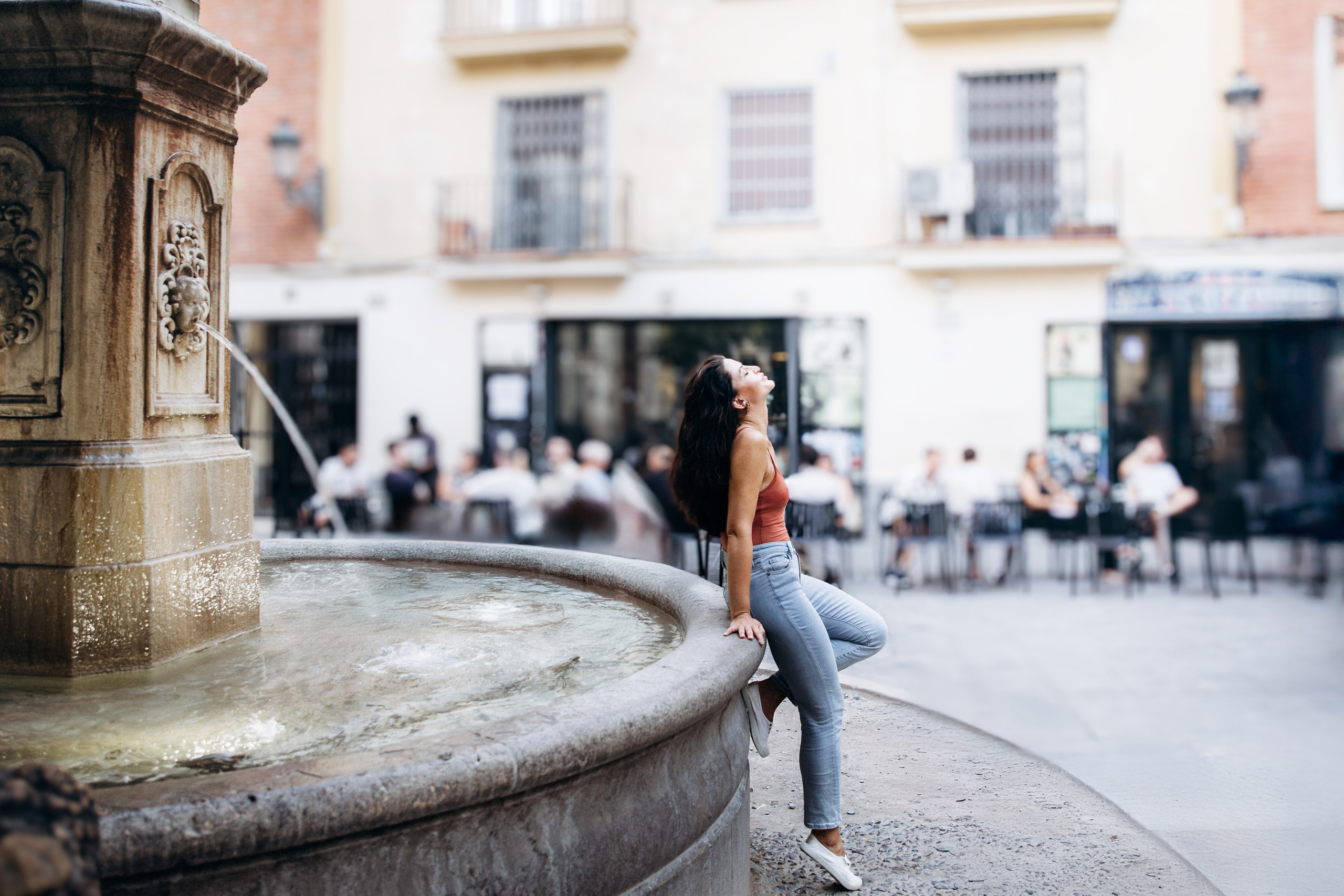 Женская фотосессия в Валенсии, Испания, где уверенная женщина позирует у исторического городского фонтана в старом городе, с естественным светом, живым движением и городской средиземноморской атмосферой — идеально для женской фотографии, лайфстайл-портретов, городских фотосессий, персонального брендинга и профессиональных женских фотосессий в Валенсии и по всей Испании.