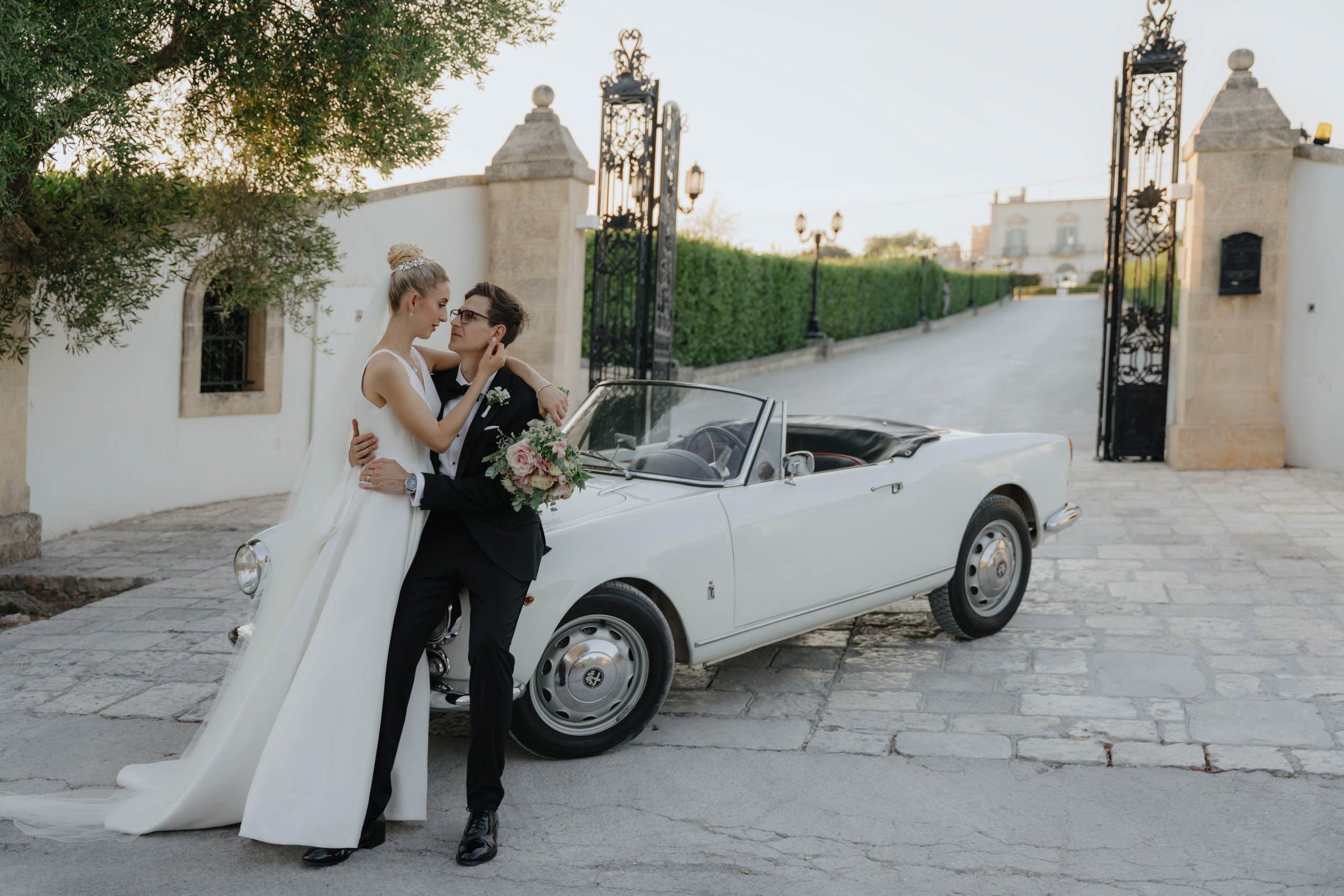 Couple posing with vintage car at sunset, luxury destination wedding photography in Italy