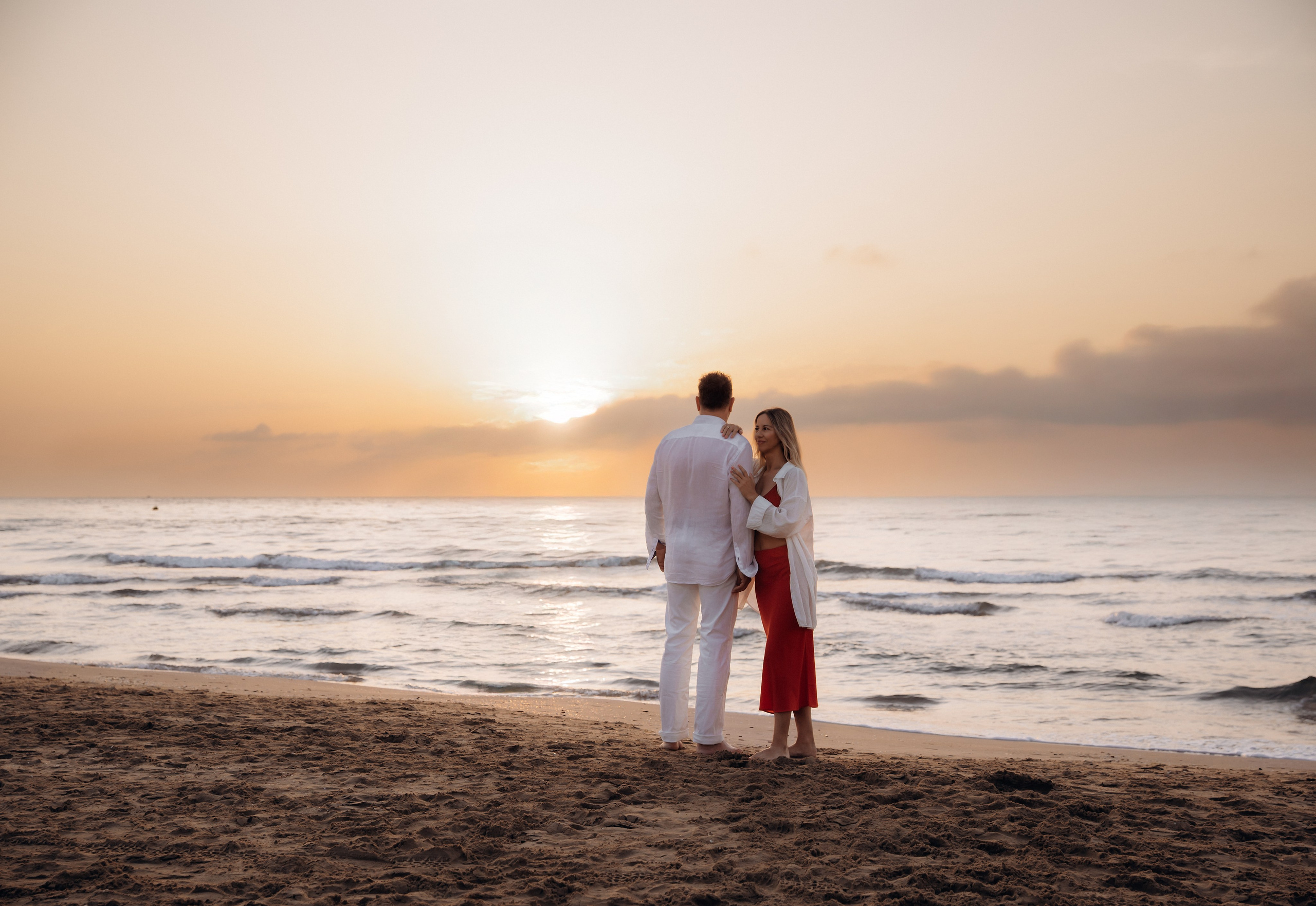 Romantic couple embracing barefoot on the beach at sunrise in Calpe, Spain — dreamy love story photoshoot capturing soft light, genuine emotion, and Mediterranean coastal serenity, ideal for couple and engagement photography sessions in Calpe and Spain.