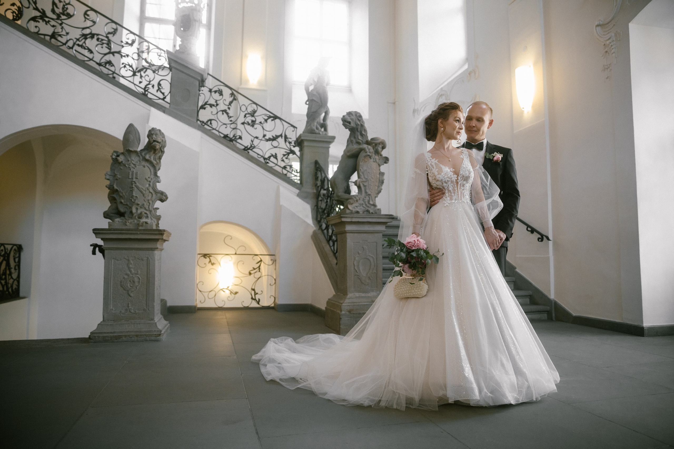 Bride and groom near statues at Schloss Meersburg, surrounded by soft natural light