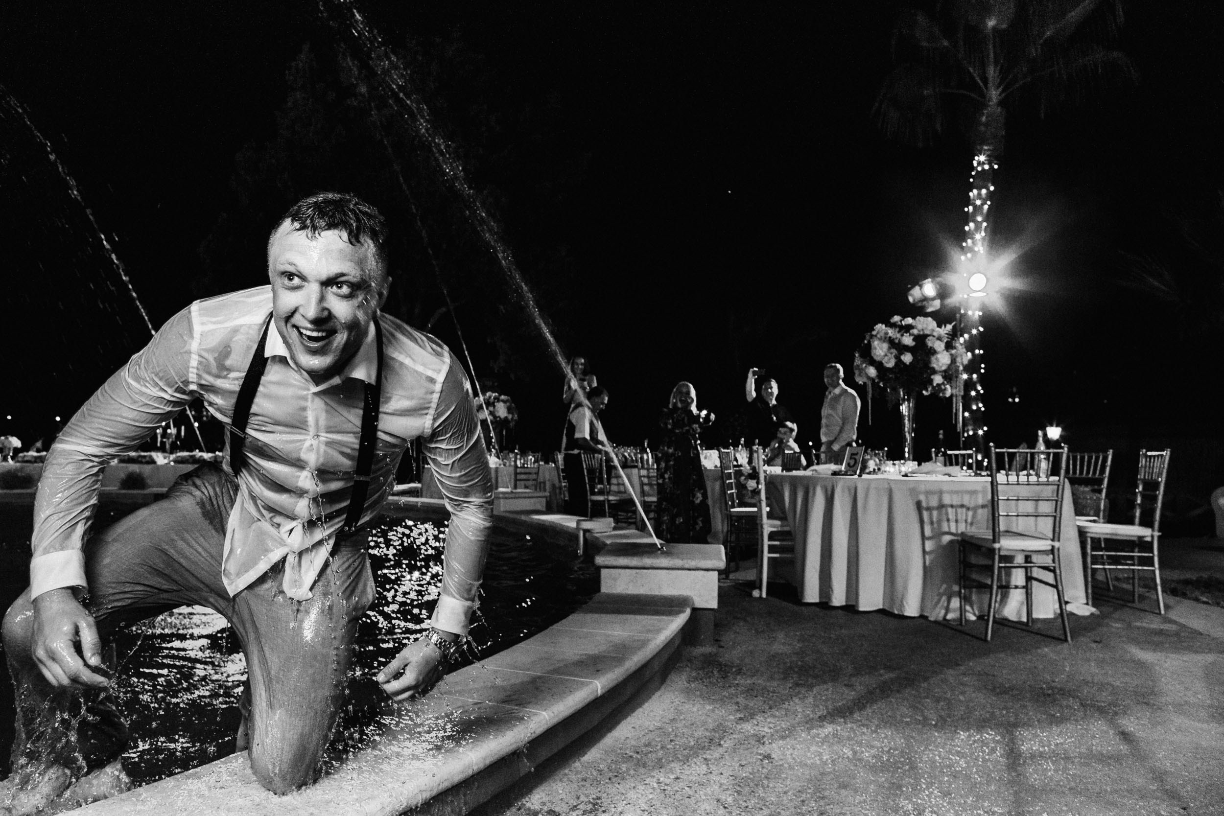 Gentleman trying to get out of the pool while fully wet and dressed in a suit