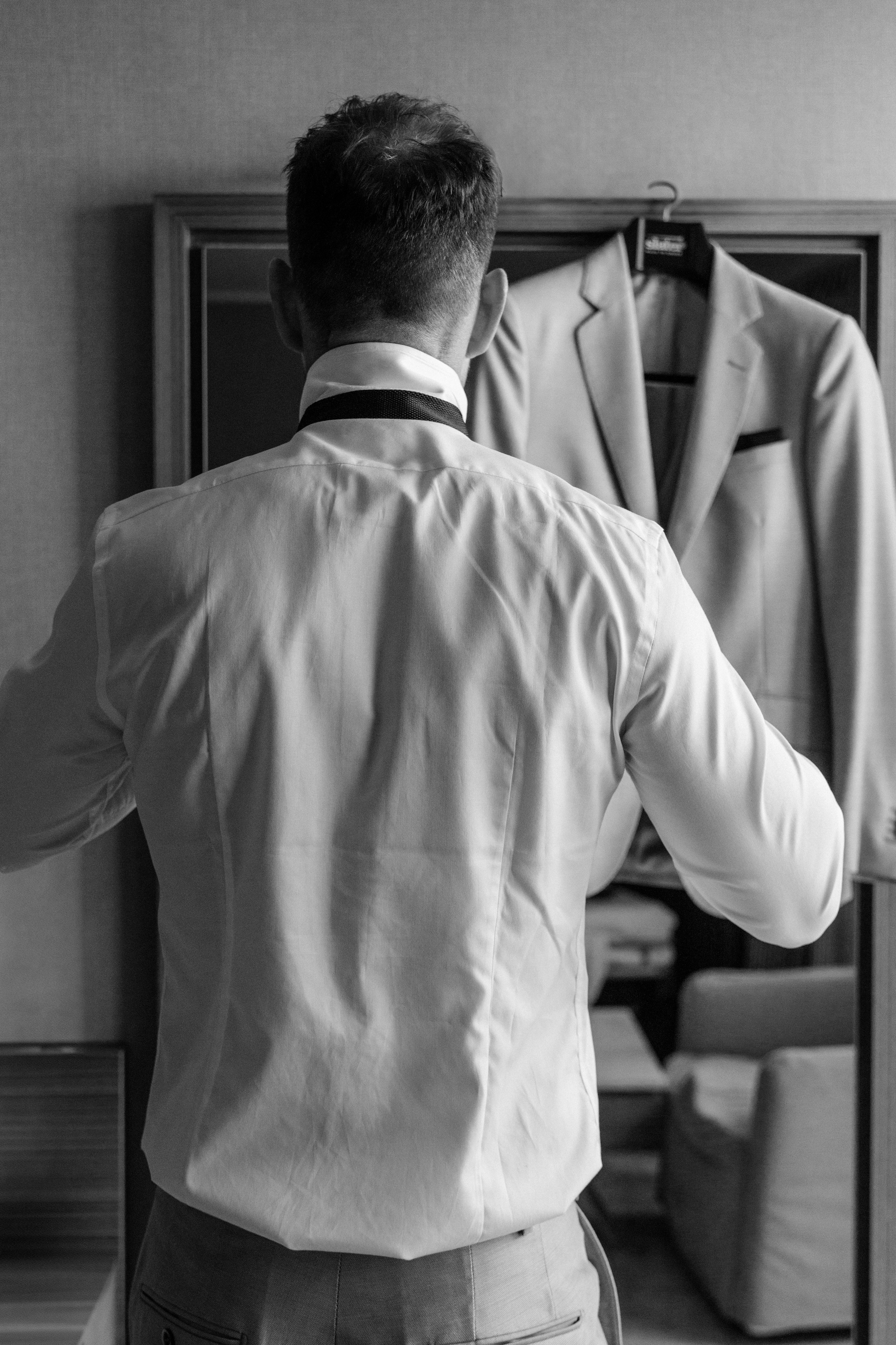 Groom adjusting his tie in front of a mirror in a luxurious hotel room in Rhodes, Greece, 