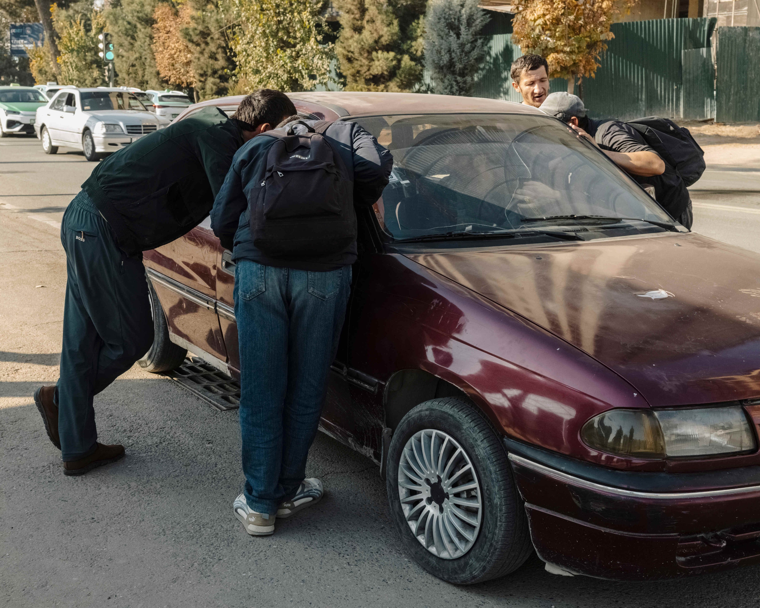 Unemployed people gather around a car to speak with an employer offering construction jobs near the city centre of Dushanbe. People wait here daily for short-term construction work, sometimes for days without success. Most have limited education and can only find basic labour jobs, often without written contracts or social protection. Projects may last from a single day to several months, and less-educated workers often struggle to secure long-term employment and report cases of underpayment or non-payment of wages. Many are former migrant workers deported from Russia.