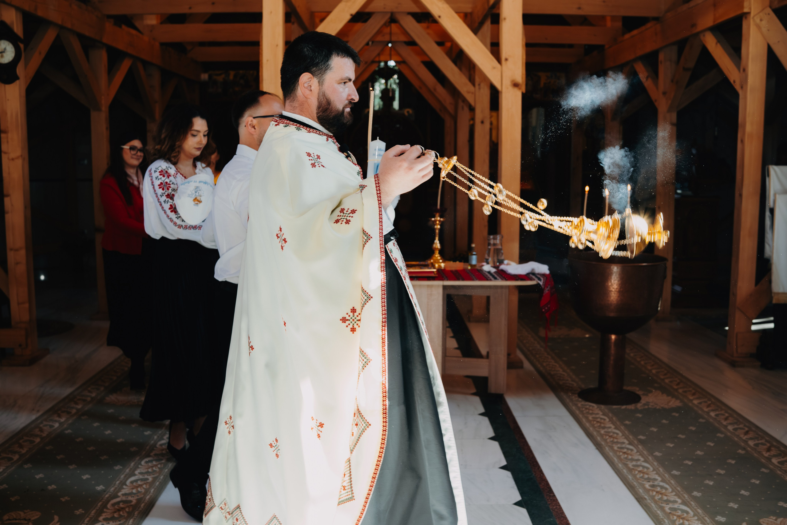 Fotografie spectaculoasă și plină de atmosferă de la botezul lui Arthur Mihail. Preotul flutură cădelnița (thurible), iar un fum dens de tămâie creează o dâră dramatică care încadrează scena în altarul Catedralei din Bârlad. Imagine plină de mișcare și simbolism.