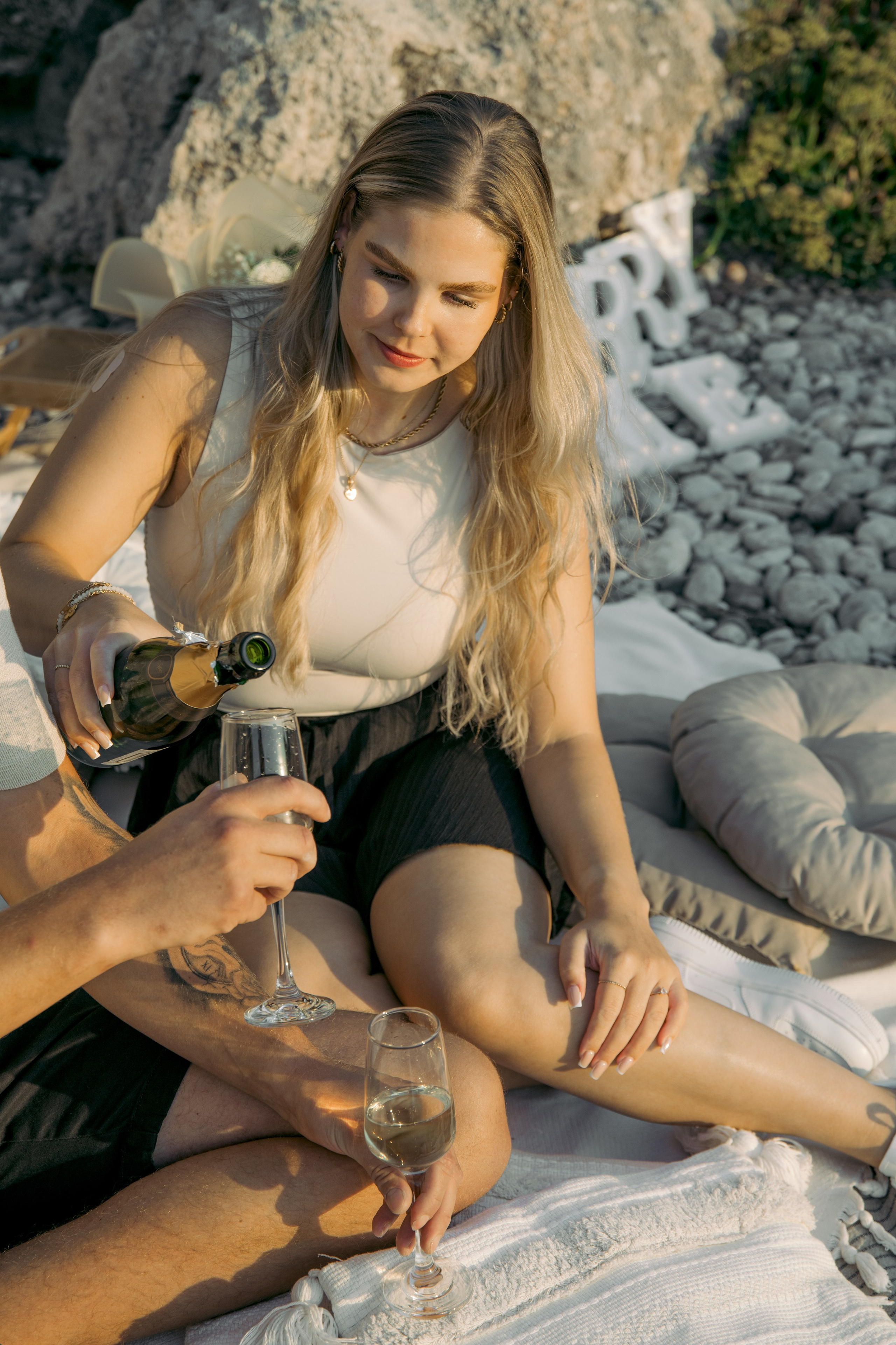 "Moment der Ruhe nach dem Ja-Wort: Ein Paar sitzt auf dem Kieselstrand von Kato Petres und genießt die Zweisamkeit. Die Wellen schlagen sanft an das steinige Ufer, und das warme Licht des Sonnenuntergangs taucht die Szenerie in goldene Farben."