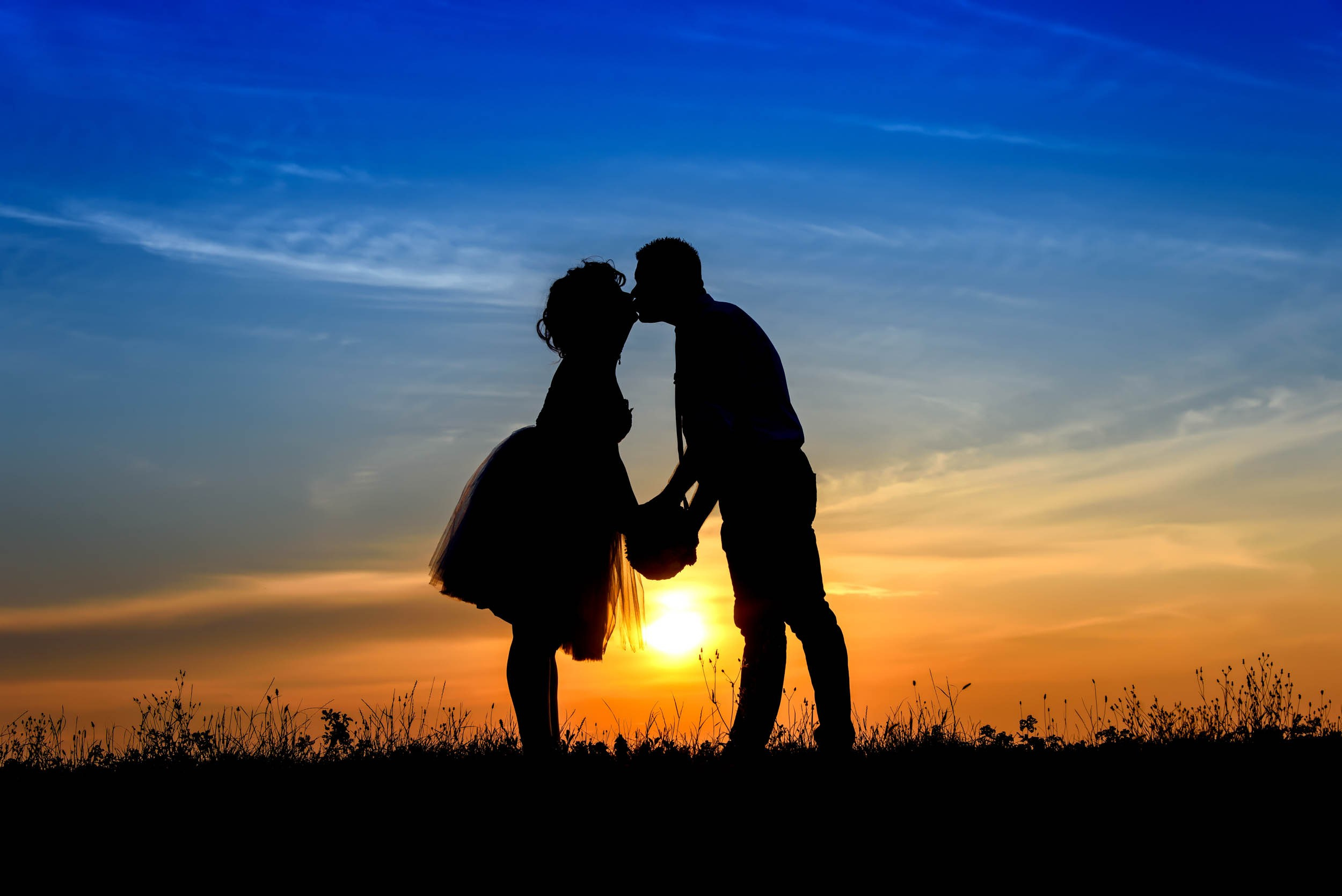 Silueta i poljubac mladenaca pri zalasku sunca sa predivnim nebom.