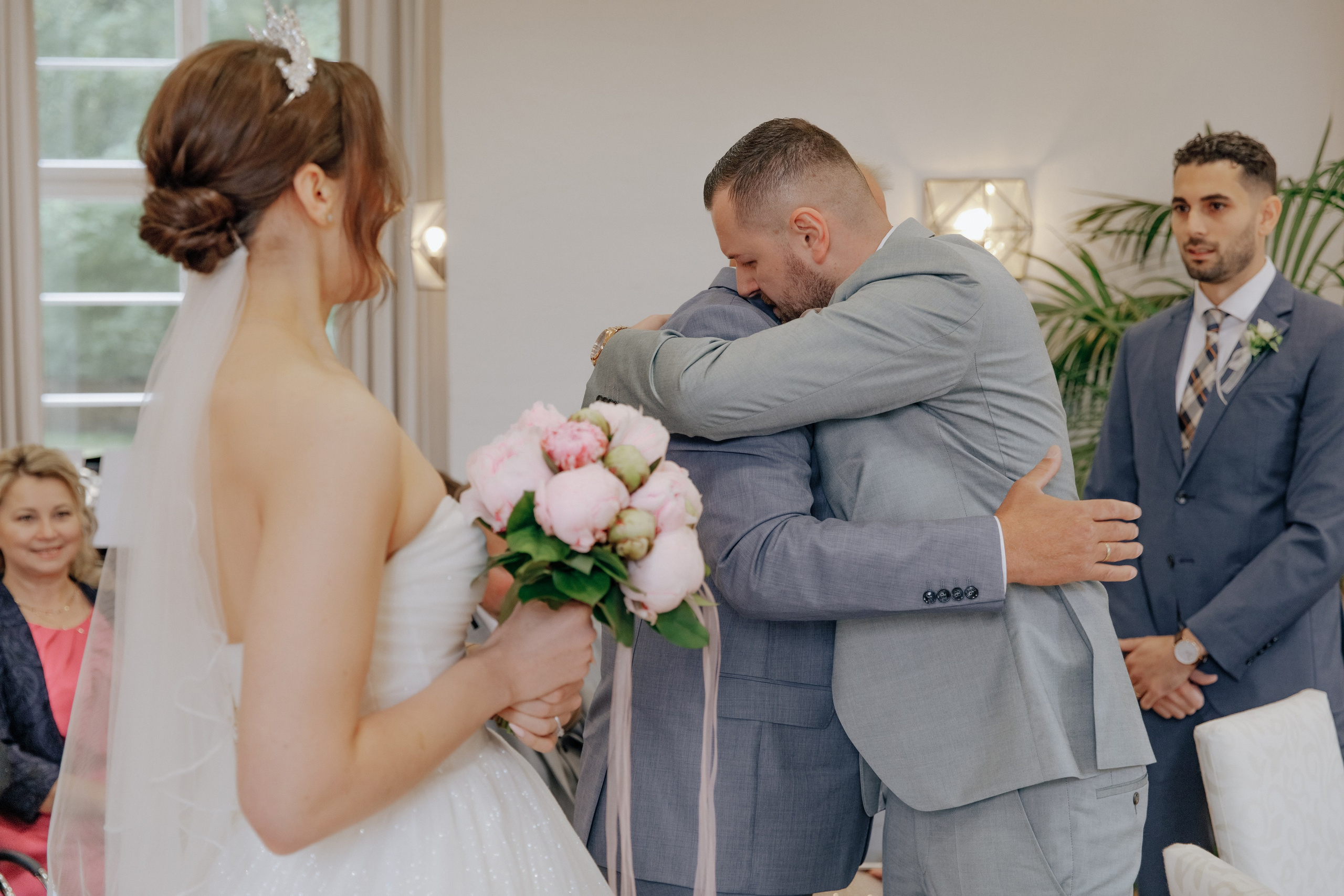 Der Bräutigam umarmt seinen Schwiegervater, während die Braut vor Rührung weint.