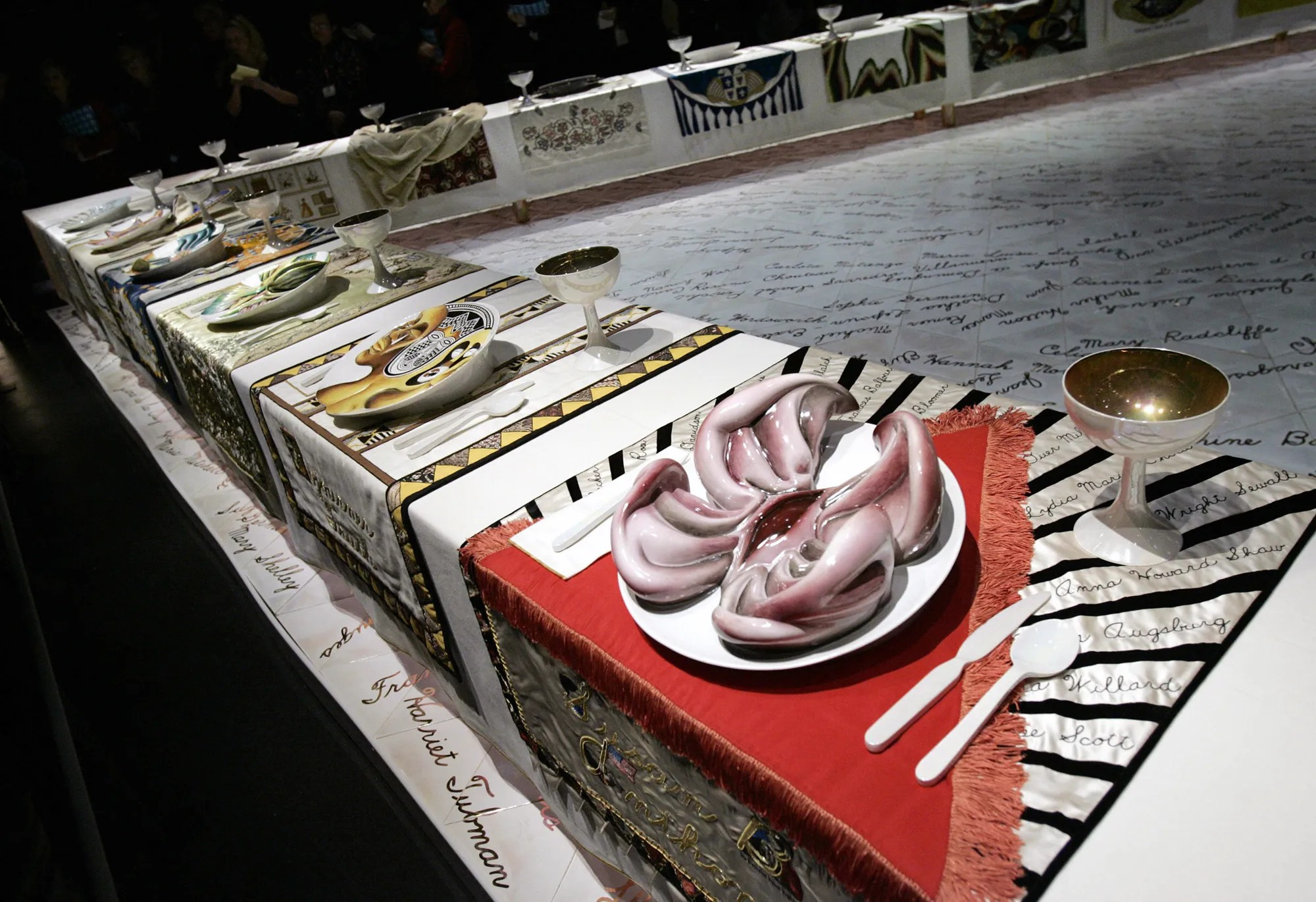 Инсталляция Judy Chicago «The Dinner Party» (1979) — треугольный стол с 39 местами, декоративными тарелками и текстильными композициями, посвященная выдающимся женщинам истории.