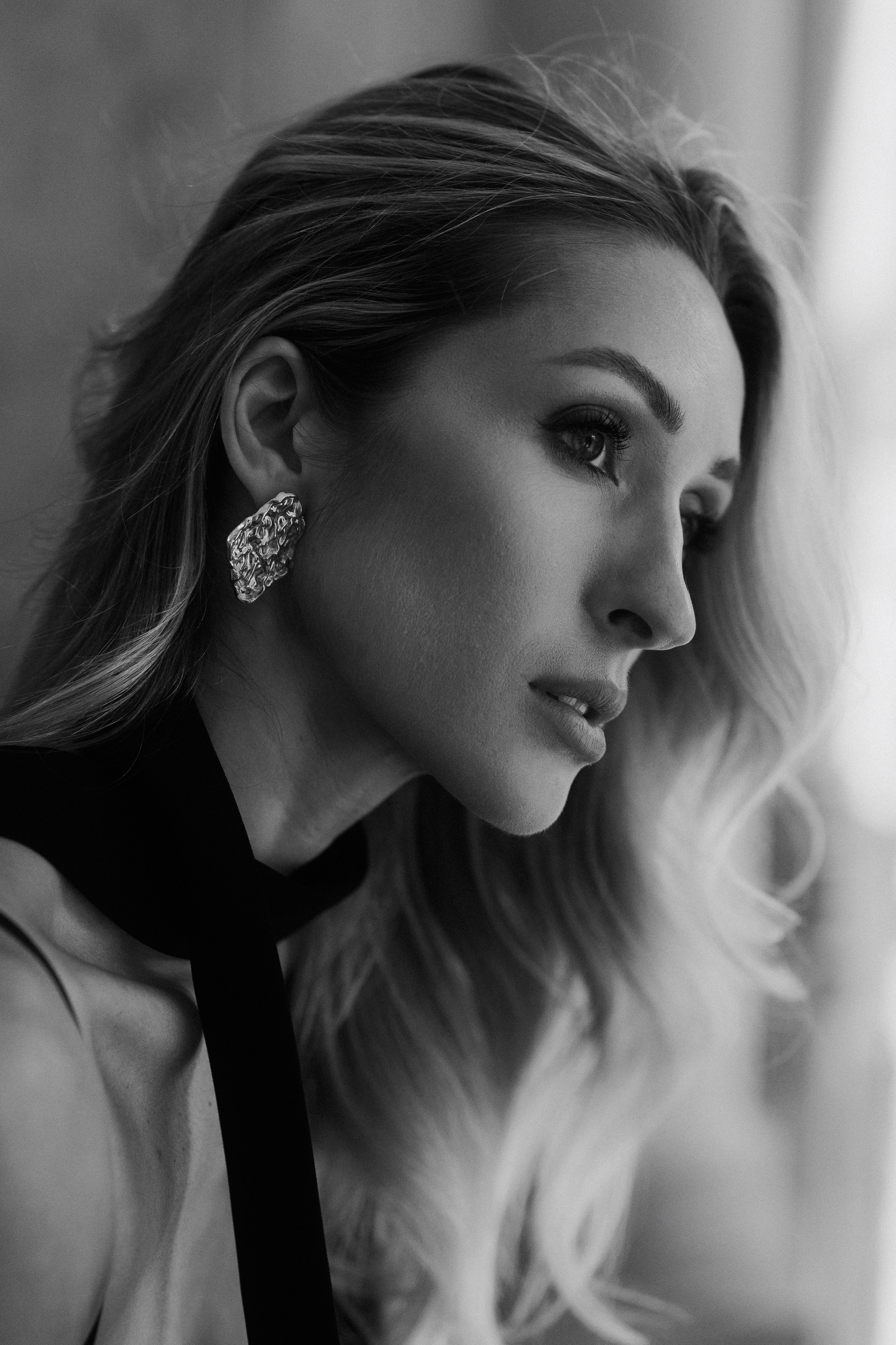 Close-up black and white profile portrait of an elegant blonde woman with statement earrings in Dresden, Germany. Fine art female portrait photography by a portrait photographer serving Dresden, Leipzig and Wurzen. Крупный чёрно-белый профильный портрет элегантной блондинки с акцентными серьгами в Дрездене, Германия. Художественная женская портретная фотография в Дрездене, Лейпциге и Вурцене.