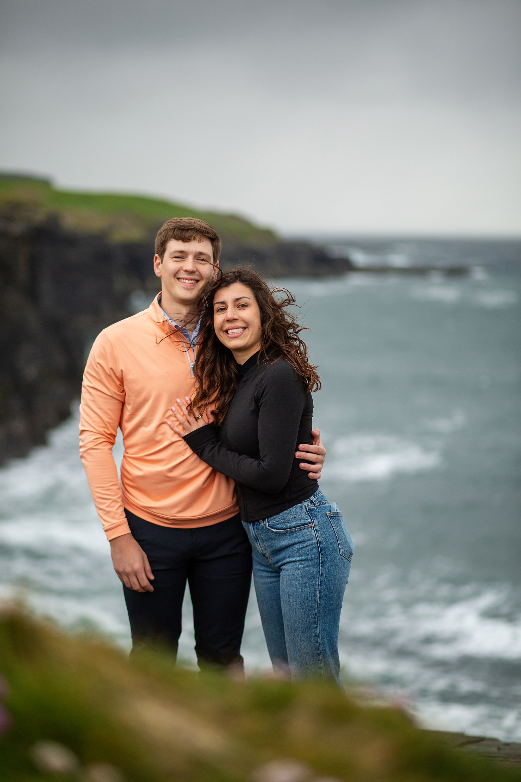 Engaged couple smiling by the Irish coastline during a natural outdoor engagement session.