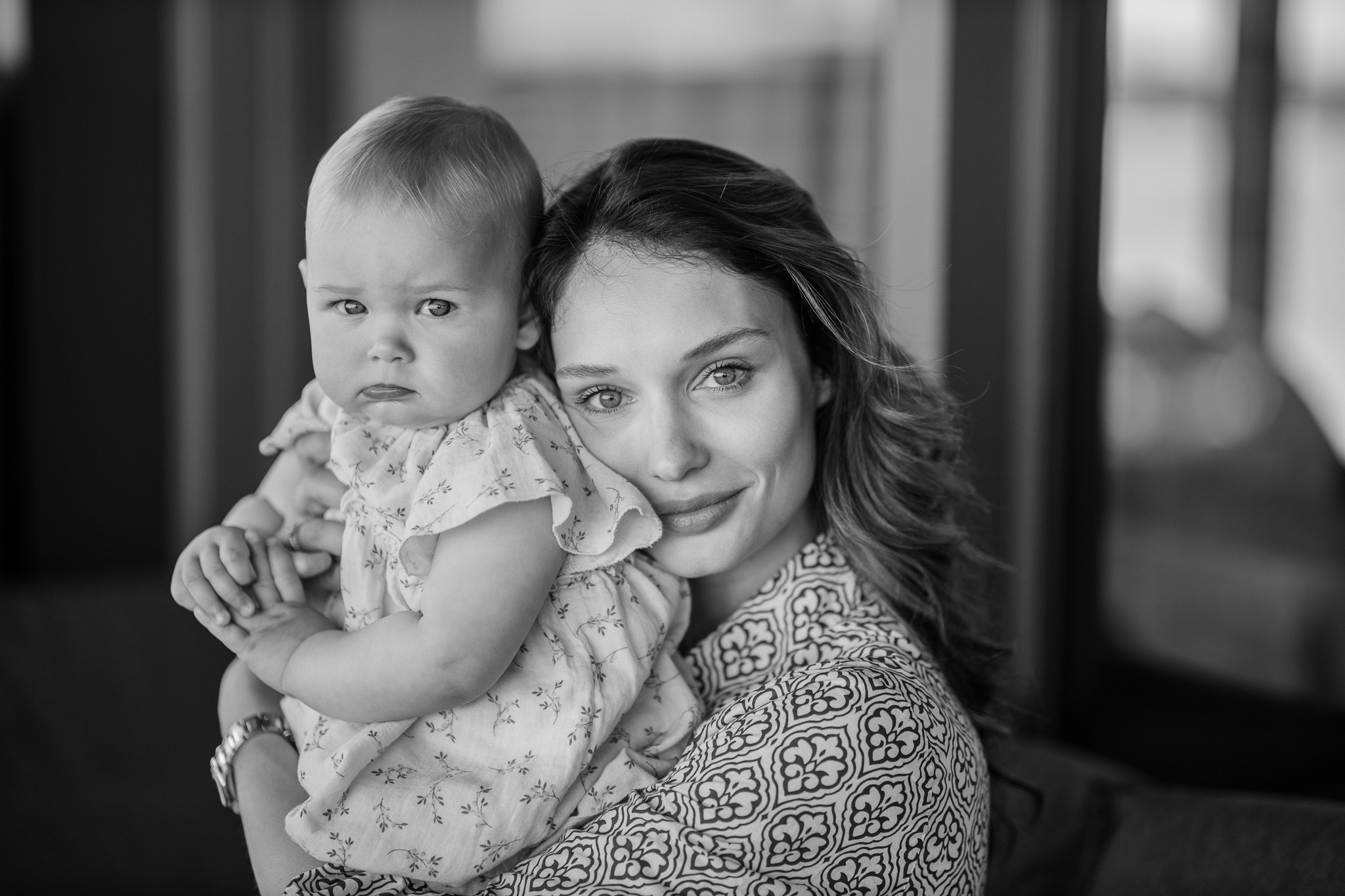 Crno-beli portret majke koja drži svoju bebu. Majka se nežno osmehuje, dok beba ima blago ozbiljan izraz lica.