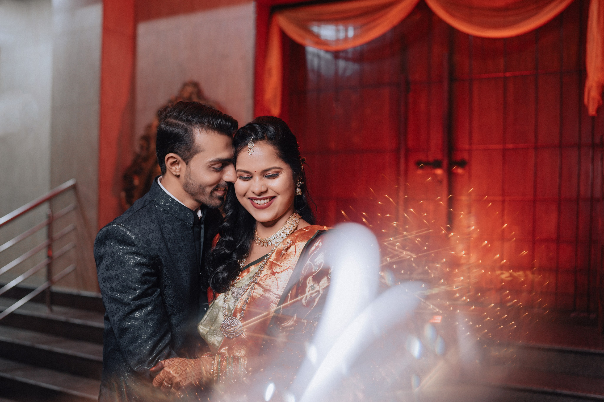 candid photograph of a smiling newly married South Indian couple embracing with celebratory special effects in a wedding hall in Malleshwaram, Bengaluru