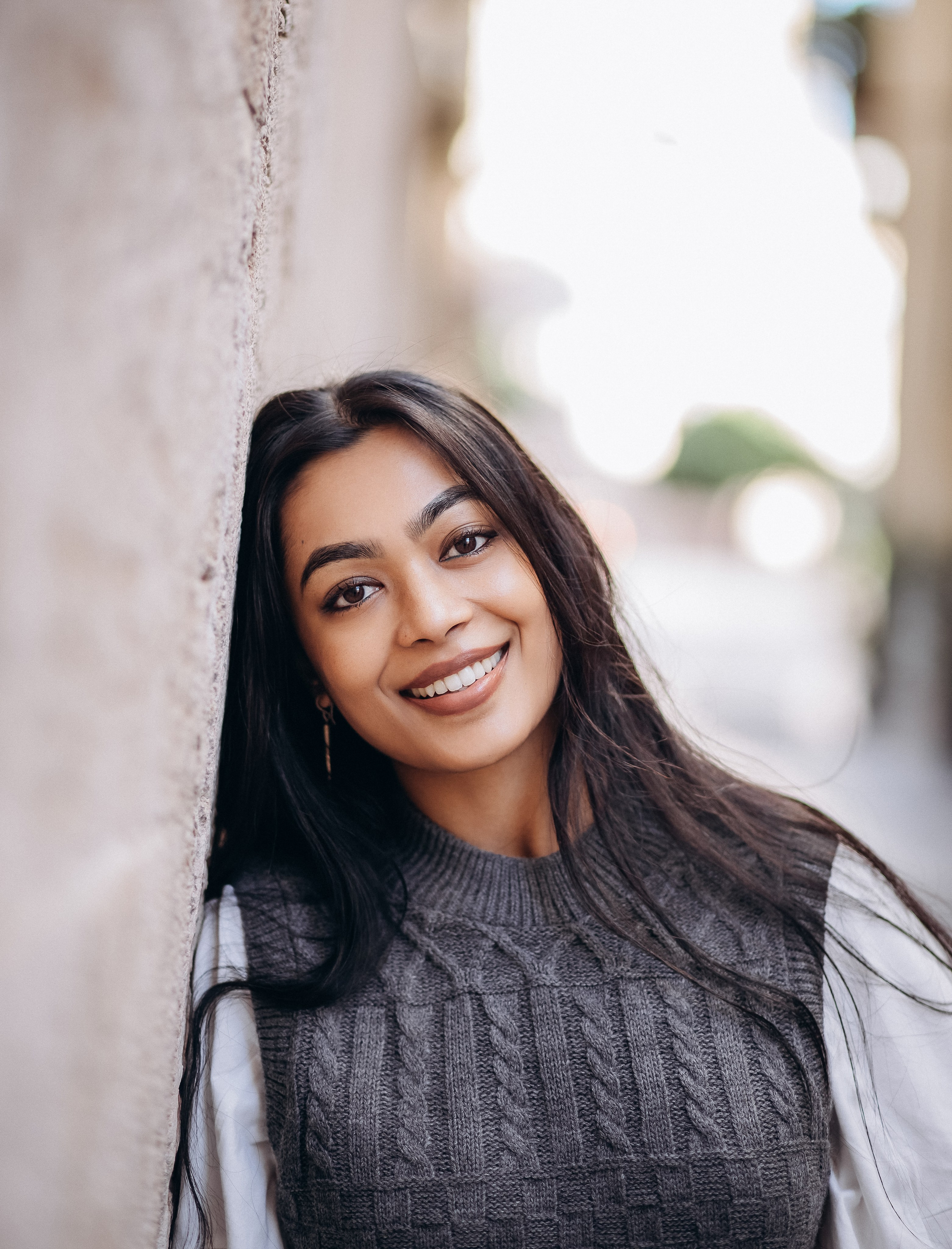 Крупный женский портрет, снятый в Валенсии, Испания — радостная женщина с естественной улыбкой, прислонившаяся к стене, залитой солнцем. Идеально для теплых и искренних женских портретных фотосессий в Валенсии и по всей Испании.