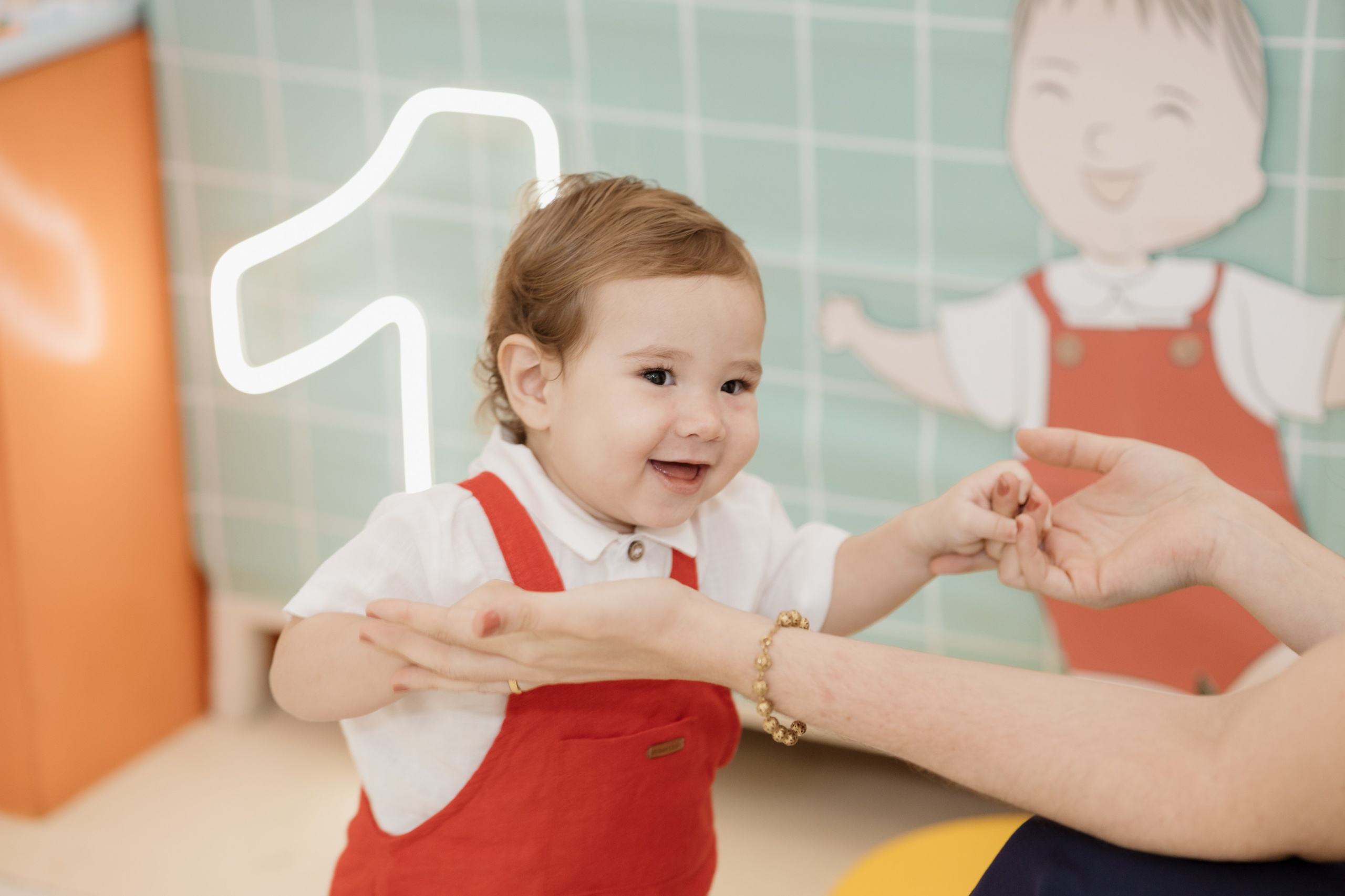 Menino segurando as mãos da mãe e sorrindo no seu aniversário de um ano