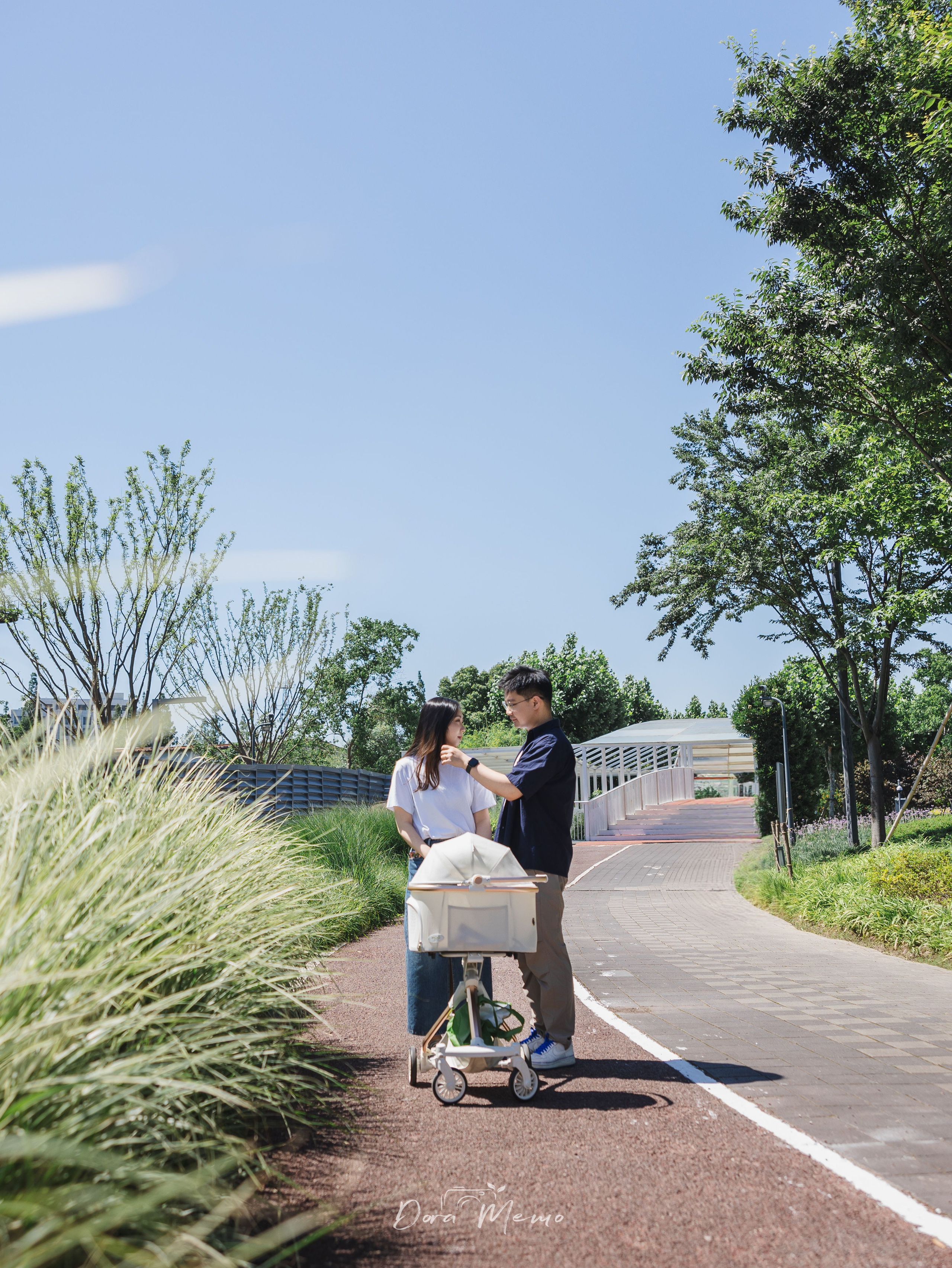Couple walking along a tree-lined park path, man's hand resting on woman's shoulder, natural lifestyle photography