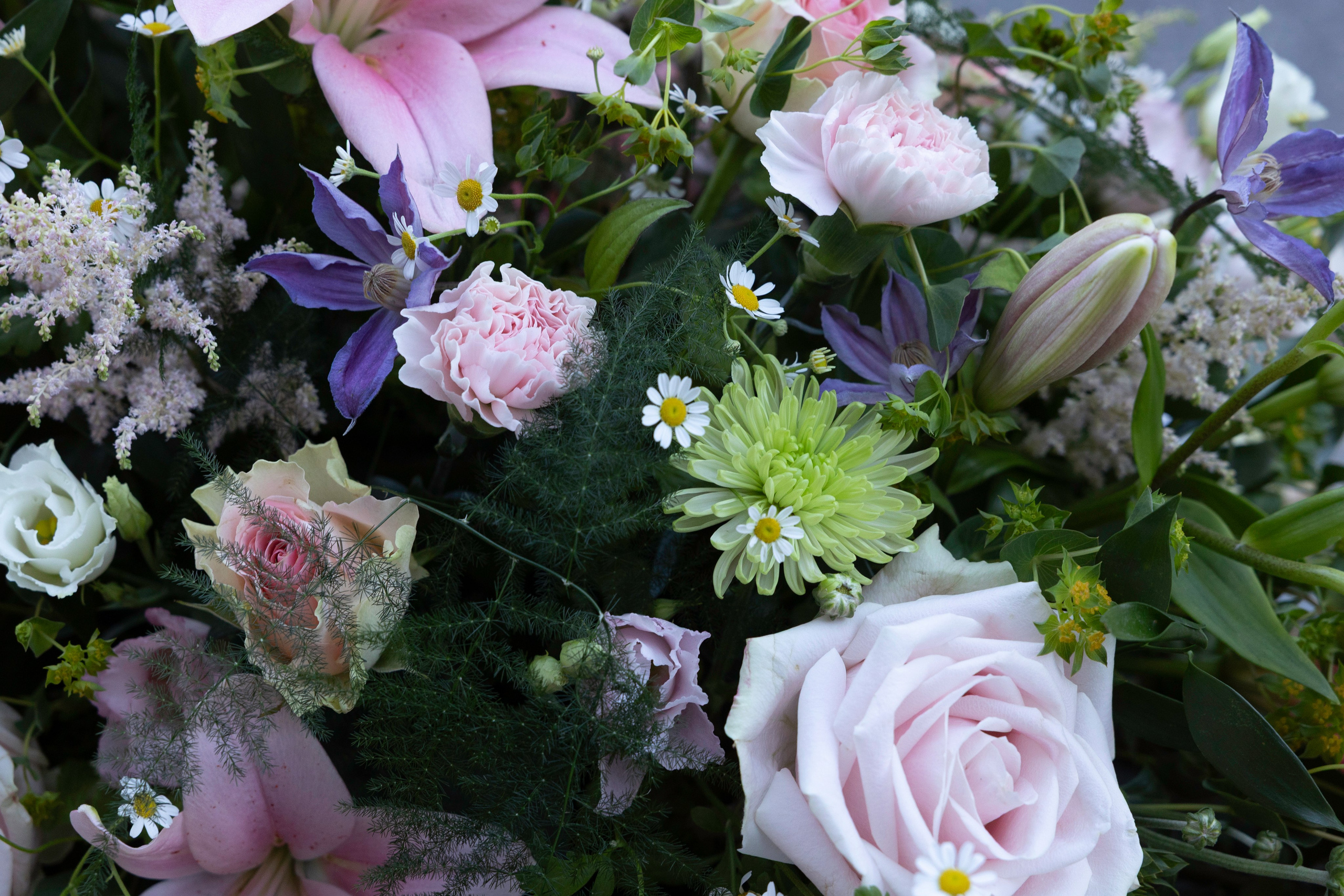 Kistepynt med elegante liljer, lyserøde roser og lette blomsterdetaljer. En harmonisk begravelsesdekoration, der forener naturlig skønhed med værdighed og omtanke.