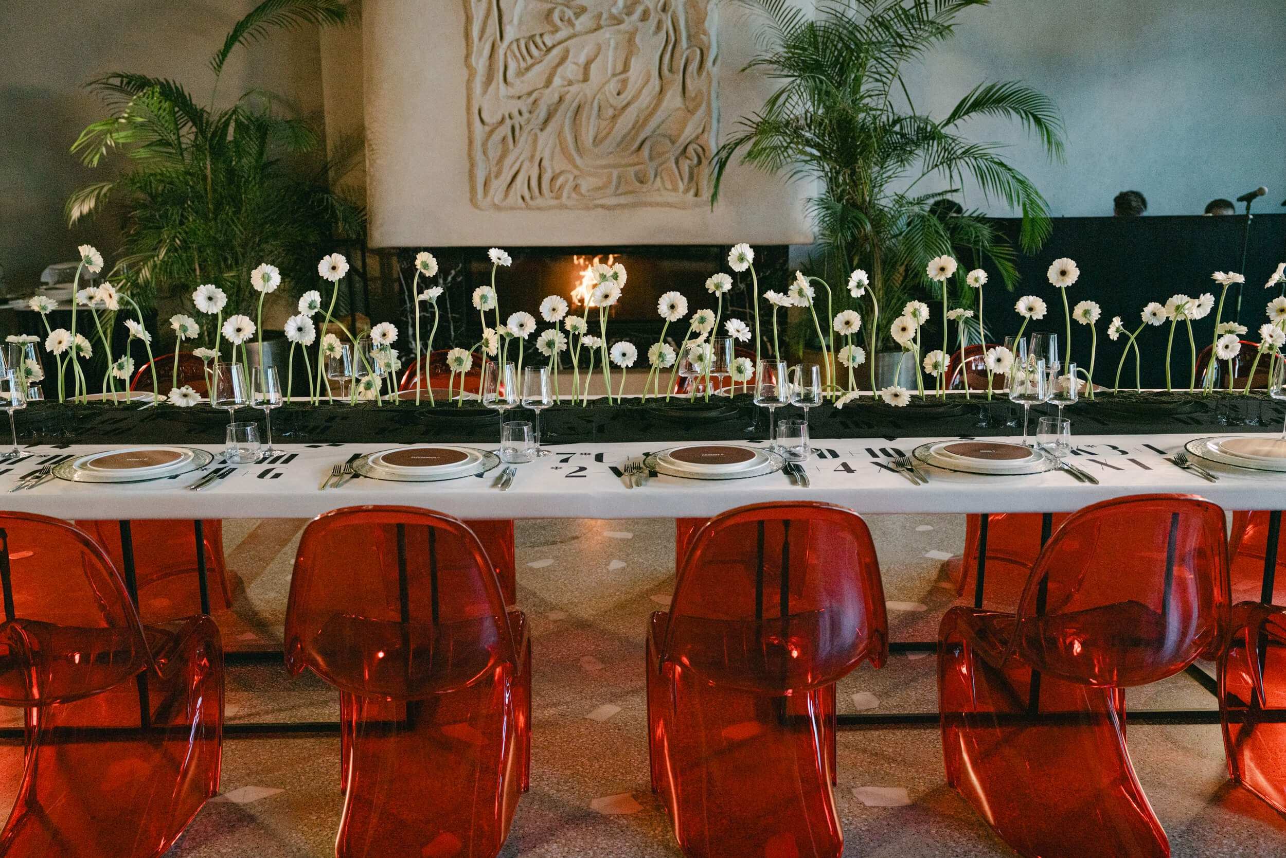 Long banquet table with flowers and red transparent chairs in a stylish Milan venue for a special occasion
