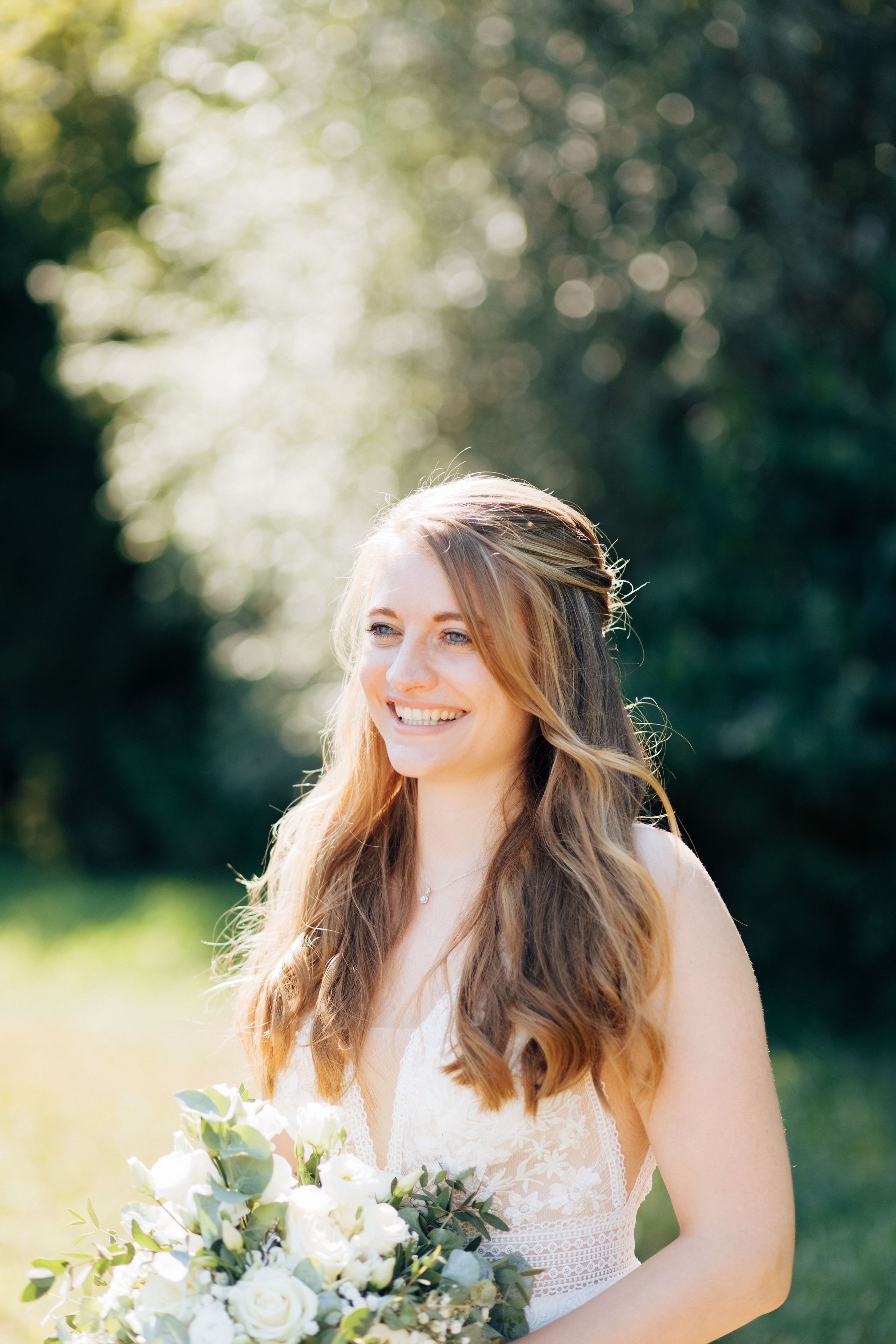 Braut lächelt mit Brautstrauß vor grünem Hintergrund.