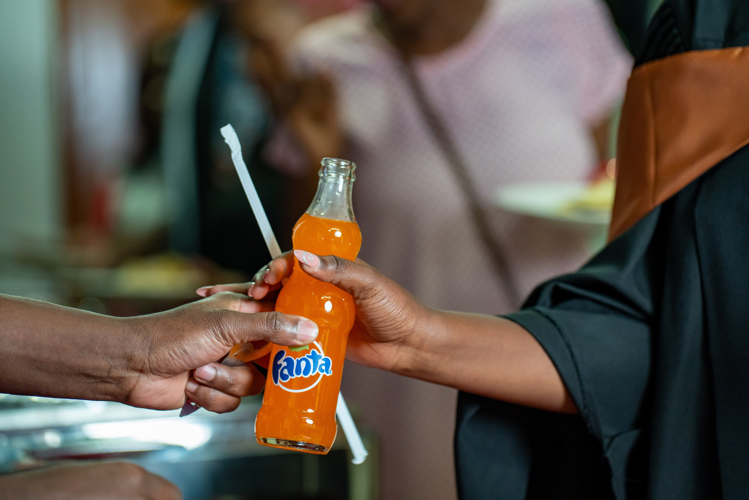 Hands exchanging orange Fanta soft drink at a graduation event – candid event photo in Kenya