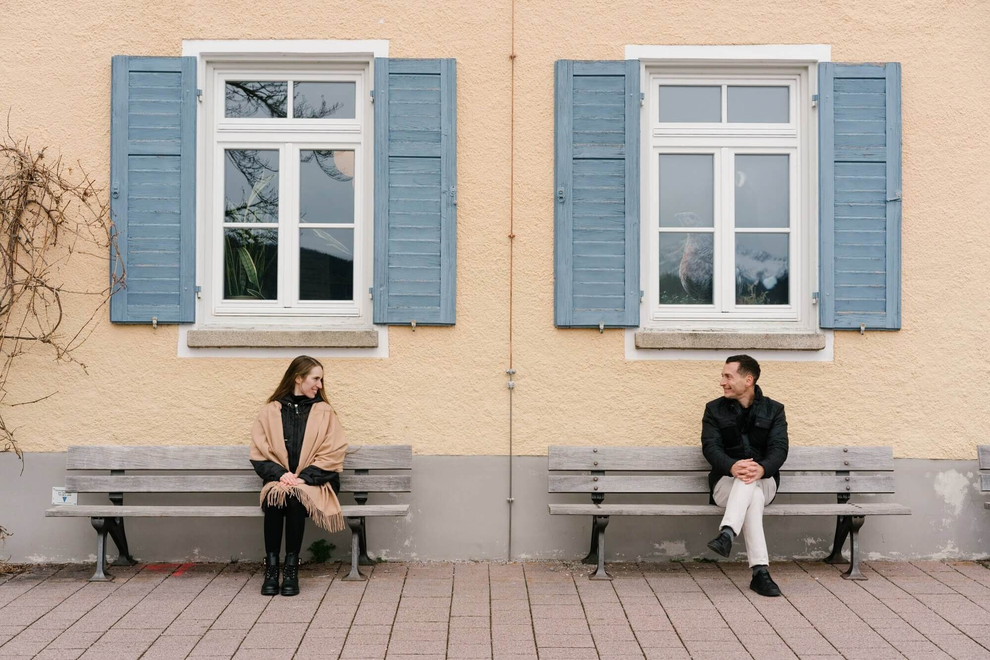 Couple sitting on a bench in front of a yellow Bavarian building with blue shutters in Tegernsee town Germany