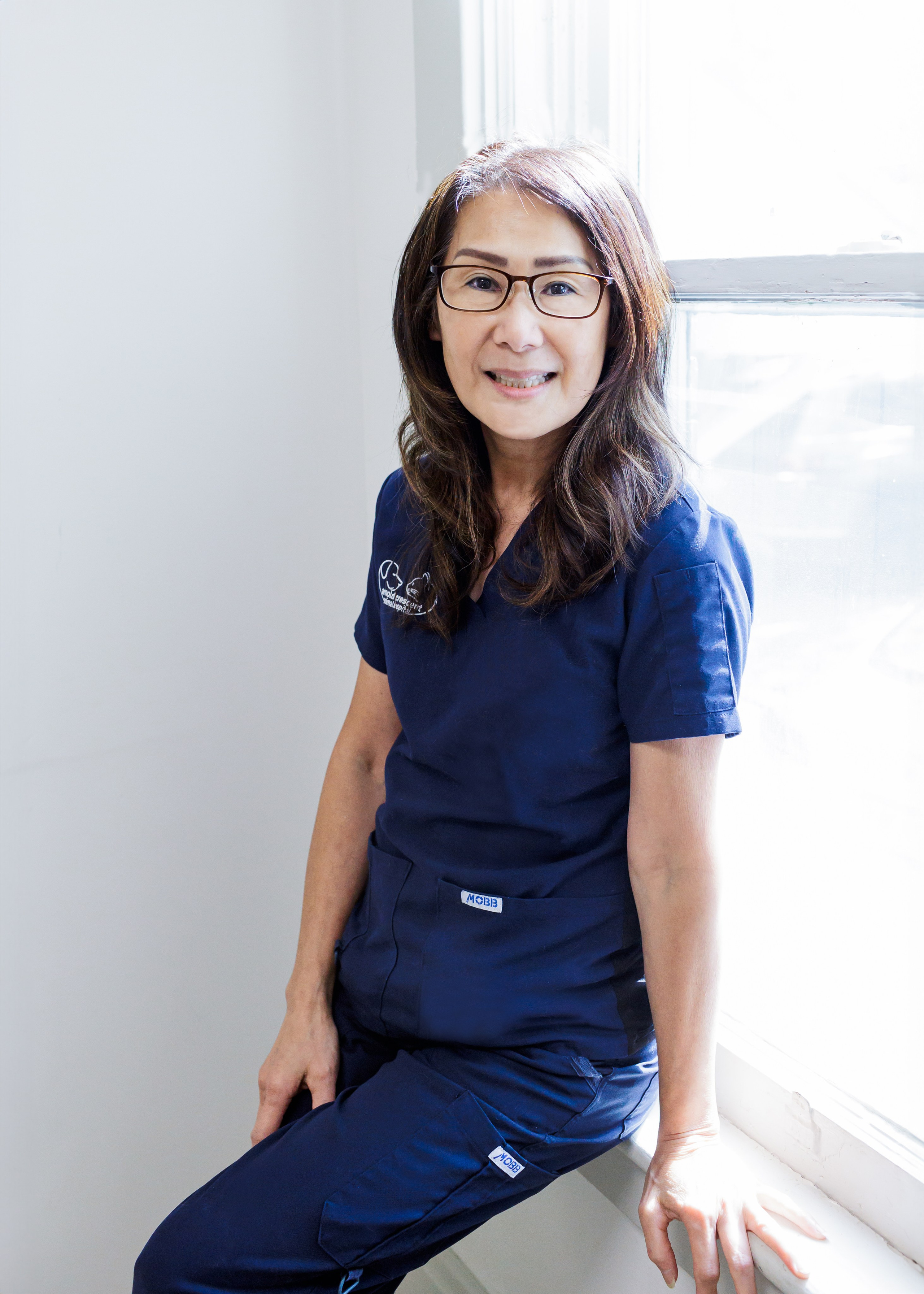 headshot of older woman in blue scrubs and glasses 