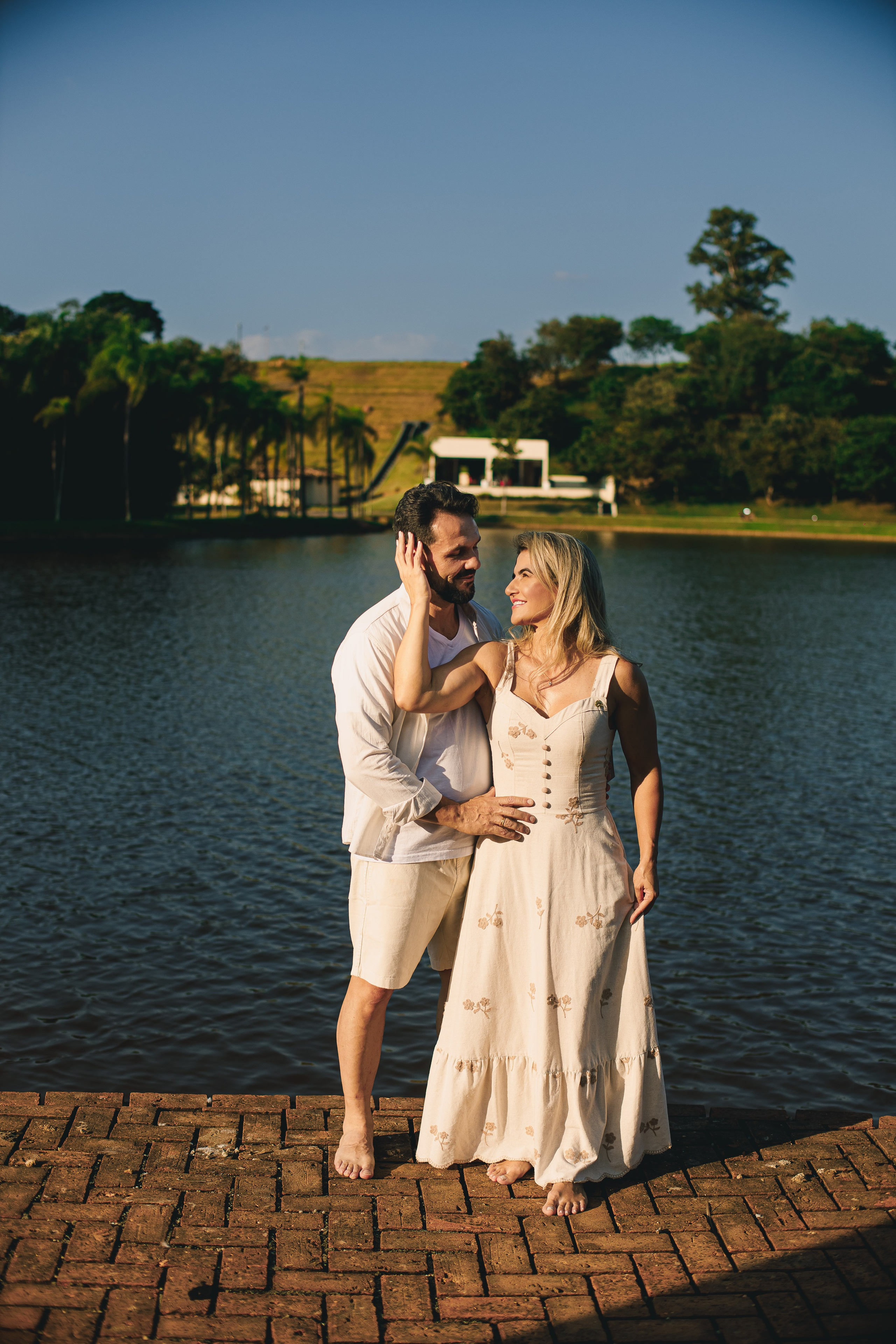 Casal se olhando apaixonados no calçadão à beira do lago do Resort das Oliveiras em Porto Feliz, com luz dourada do fim de tarde