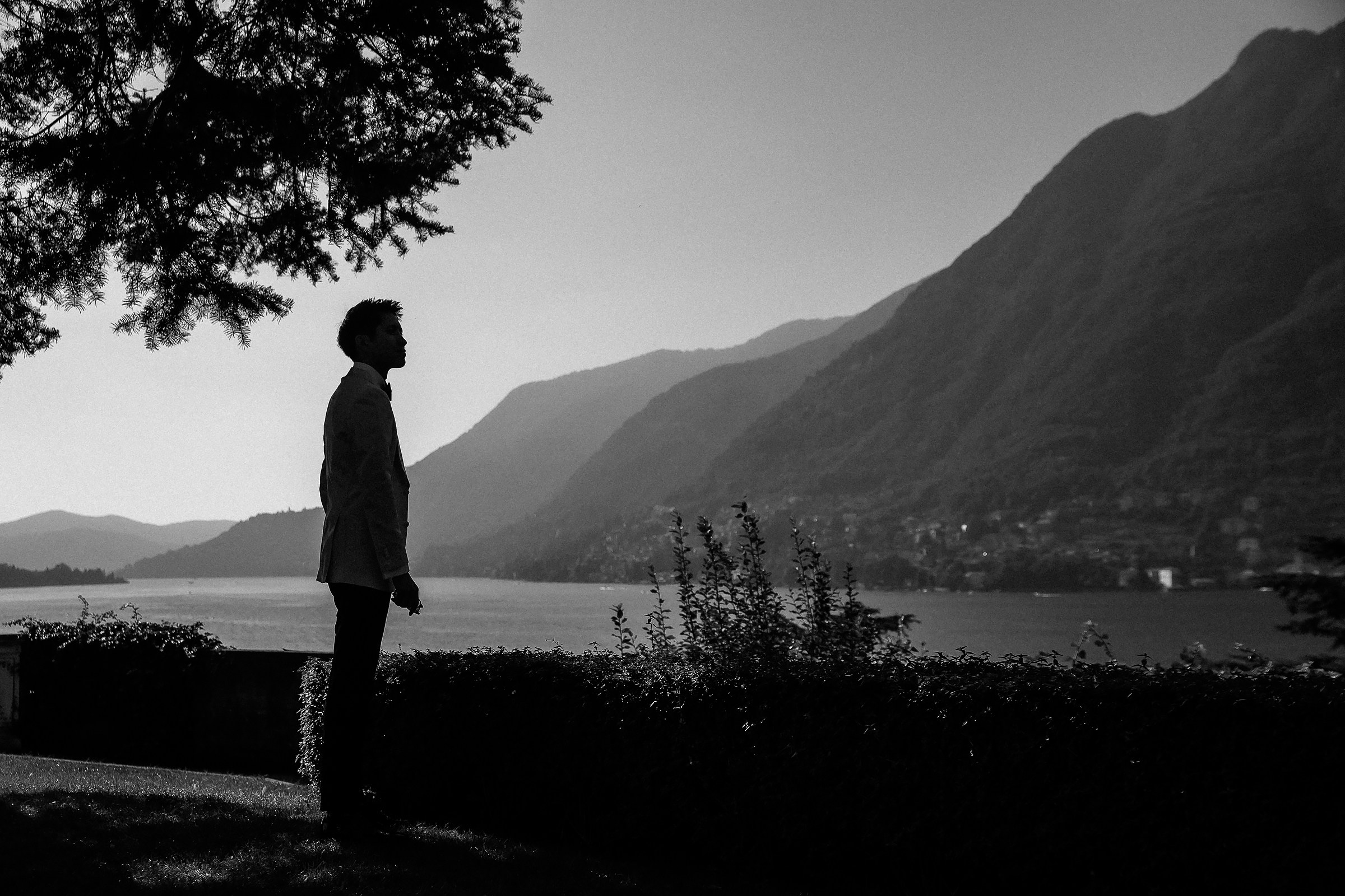 Silhouette of a groom looking over Lake Como against a backdrop of mountains.