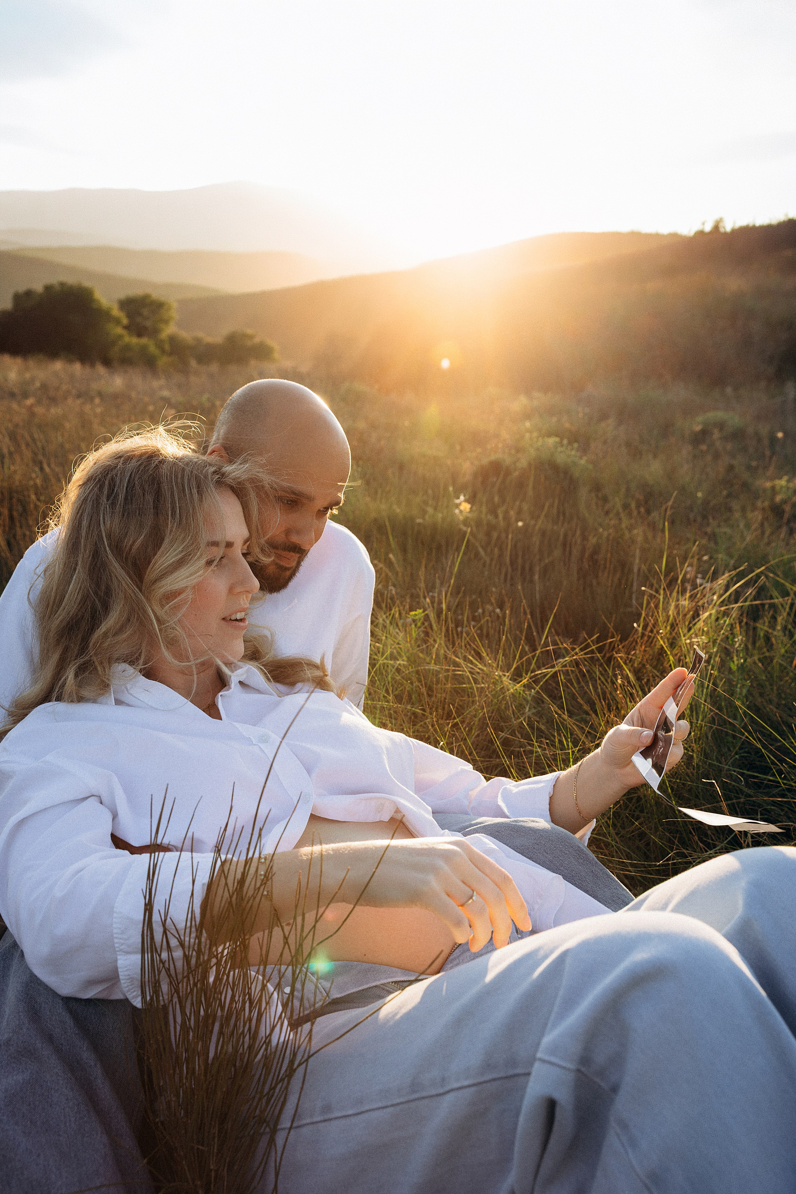 Sesión de fotos de embarazo en Valencia, España, con una mujer embarazada junto a su pareja en un paisaje natural al atardecer, capturada con cálida luz dorada para un momento íntimo y cinematográfico — ideal para sesiones de embarazo y maternity en Valencia y en toda España.