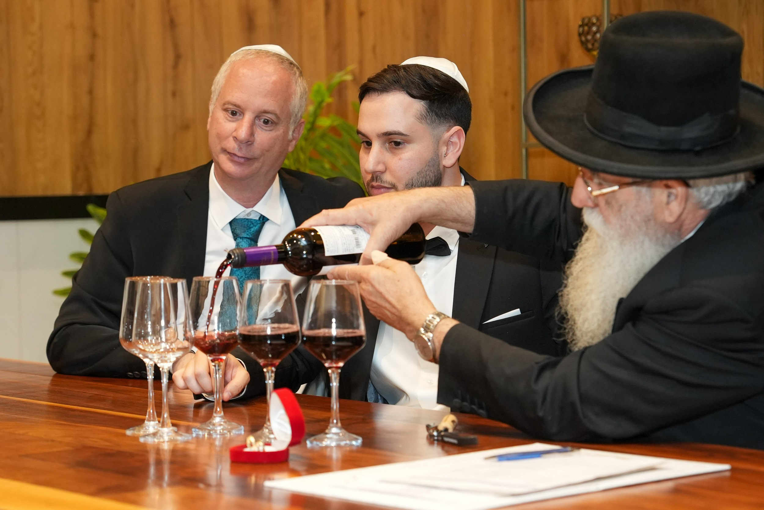 Groom Ron and his father watching a rabbi pour wine during the traditional Ketubah signing ceremony at 88 Event Garden in Emek Hefer, Israel