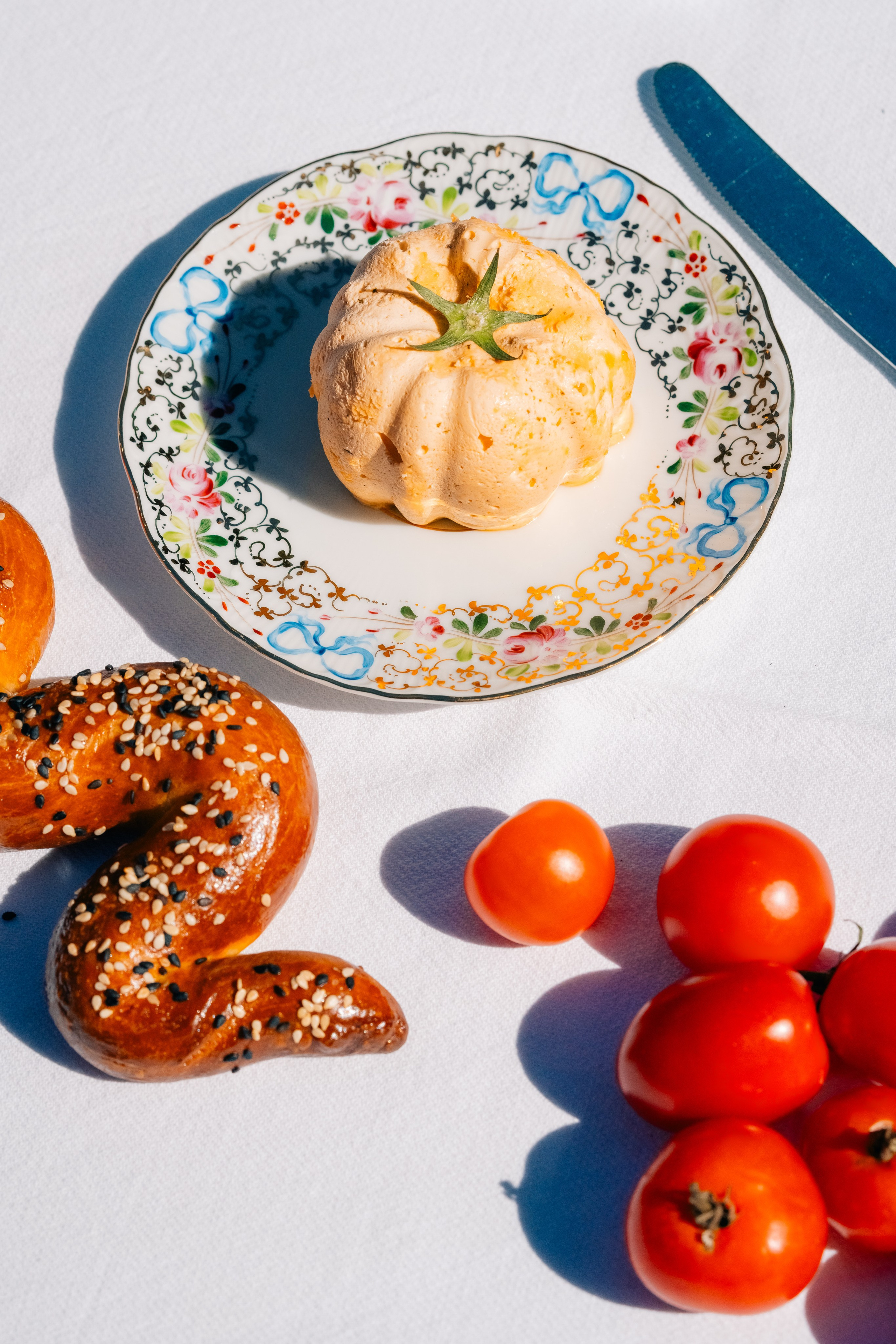 Красочная композиция с выпечкой, помидорами и хлебной закруткой. Яркая сервировка стола с выпечкой на декоративной тарелке, свежими помидорами черри и хлебной закруткой, покрытой кунжутом.