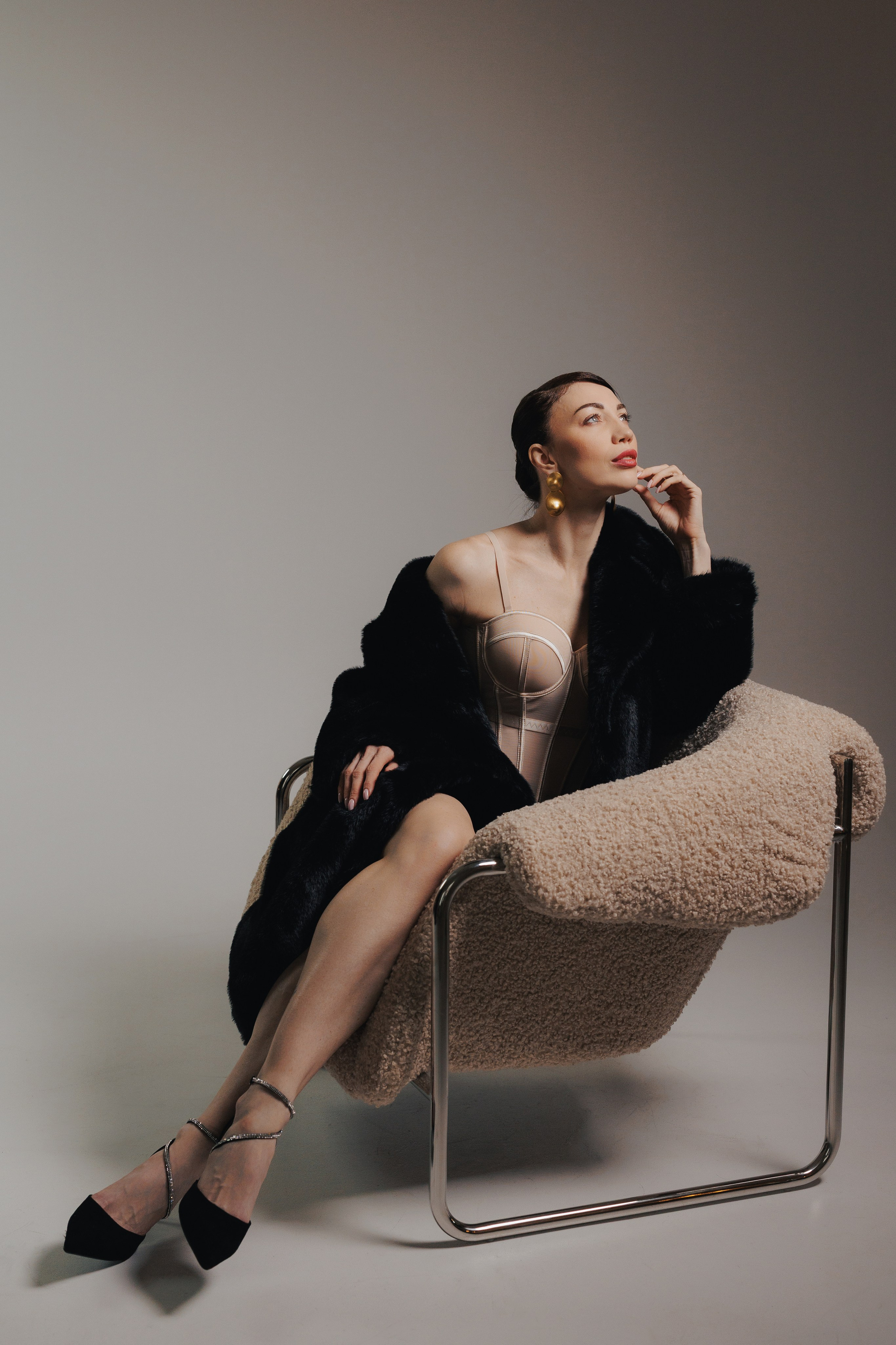 Editorial fashion portrait of a woman in a black fur coat sitting in a modern chair with elegant pose, photographed in Leipzig, Germany. Редакционный фэшн-портрет девушки в чёрной шубе, сидящей в современном кресле в элегантной позе, снятый в Лейпциге, Германия.