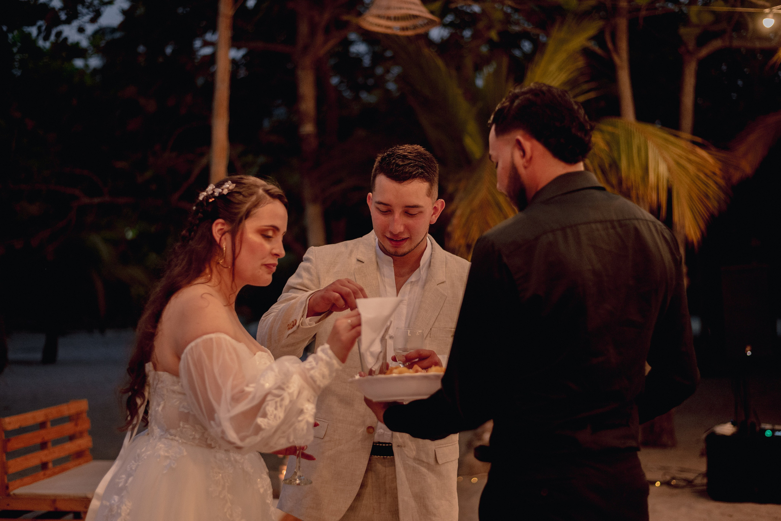 Fiesta de noche en boda playa tropical, pareja con invitados en ambiente de celebración