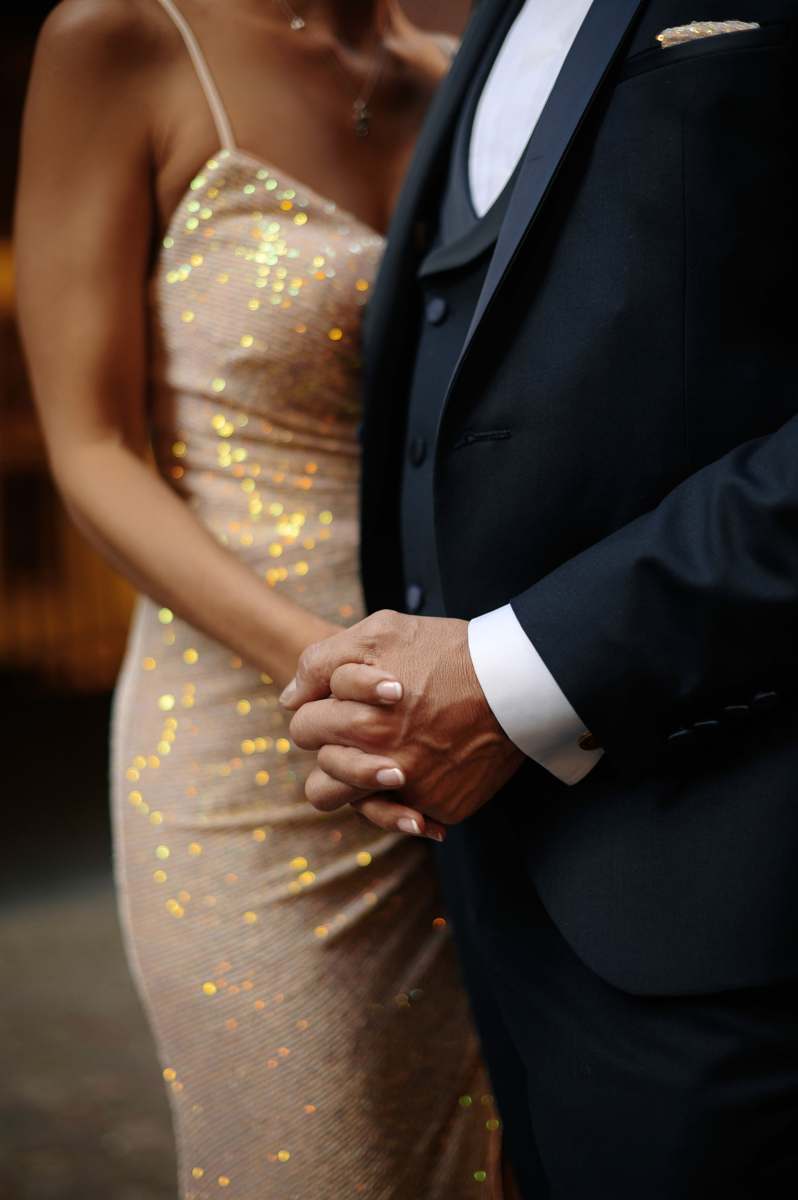 Detailfoto der Hände eines Brautpaares mit glitzerndem Brautkleid und elegantem Anzug
