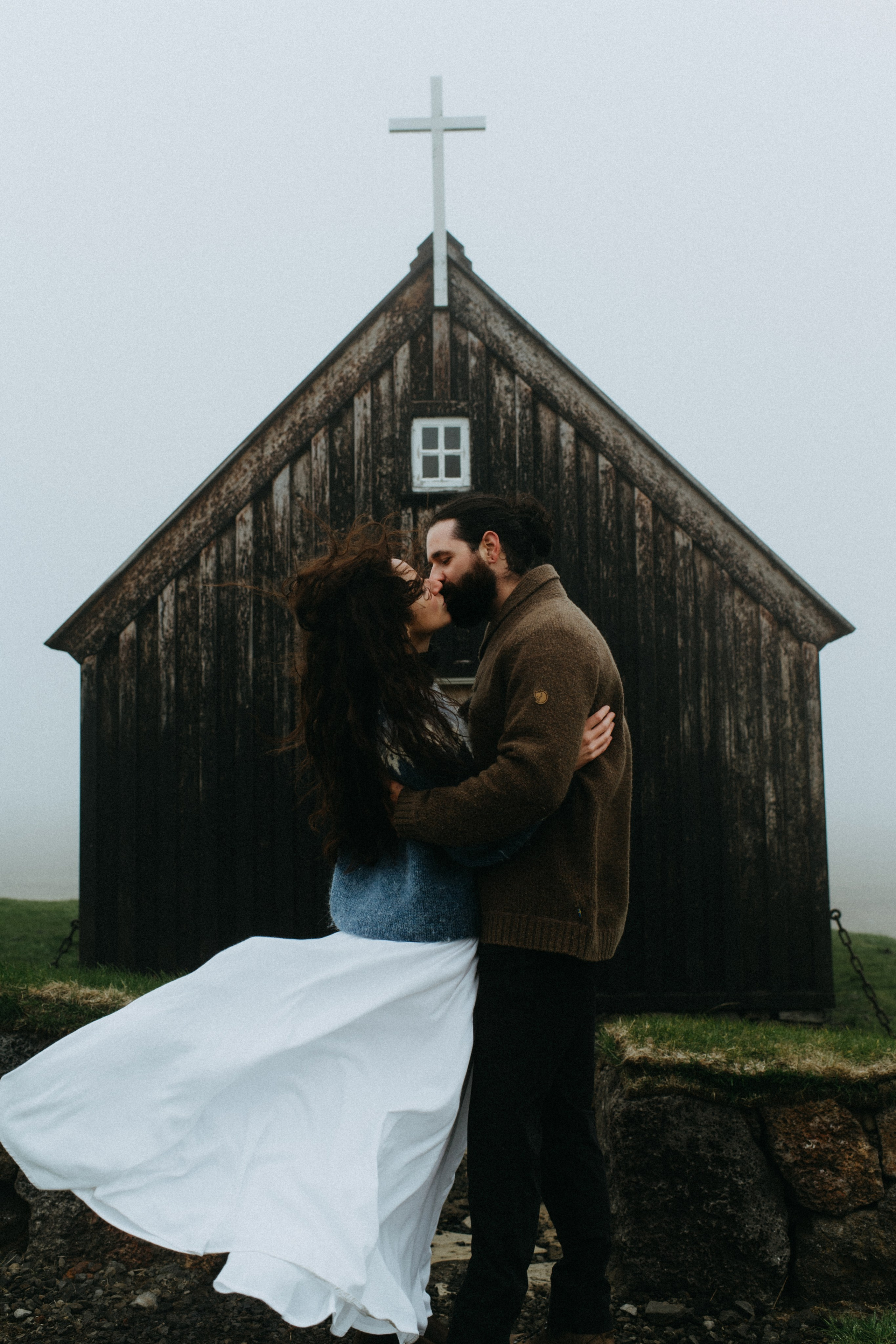 Bride and groom standing in front of the historic Krýsuvíkurkirkja, with dark clouds adding to the dramatic atmosphere.