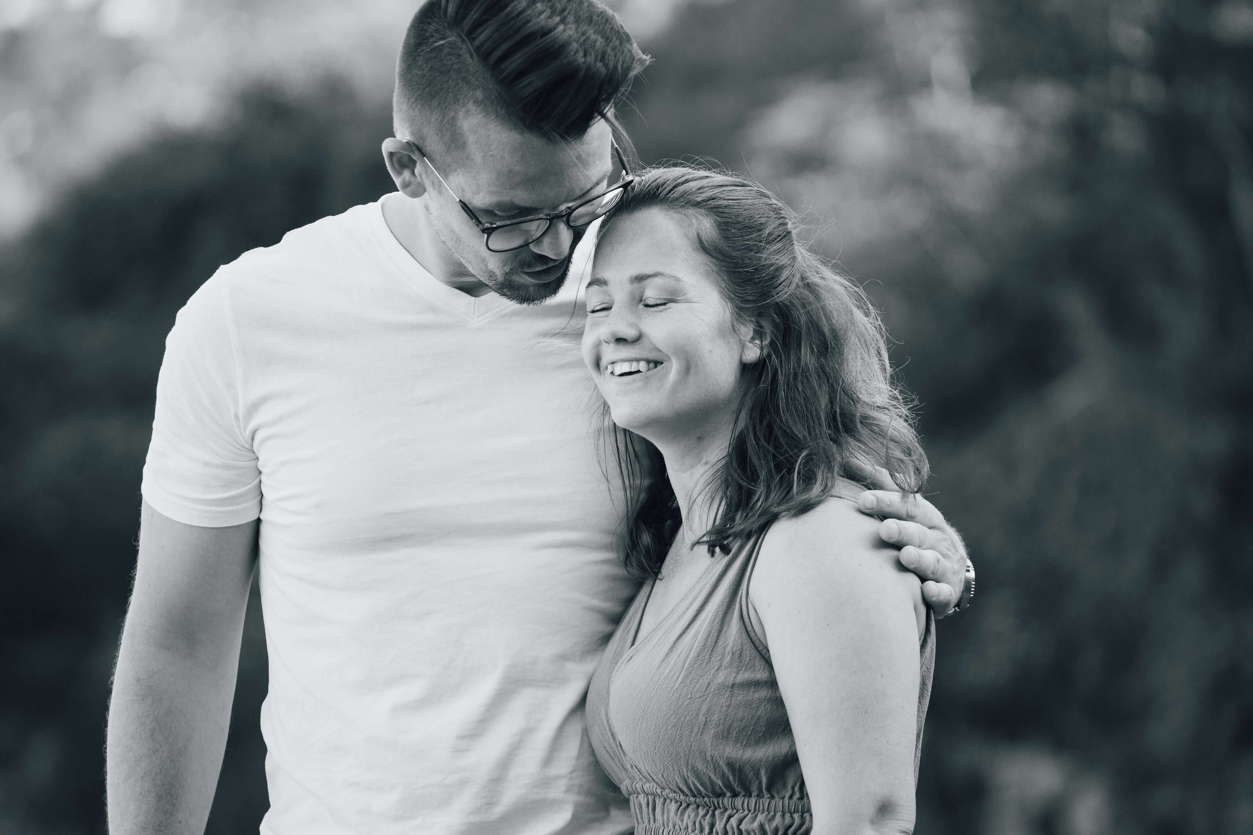 Mor og far smiler og holder hverandre mens barna leker rundt dem