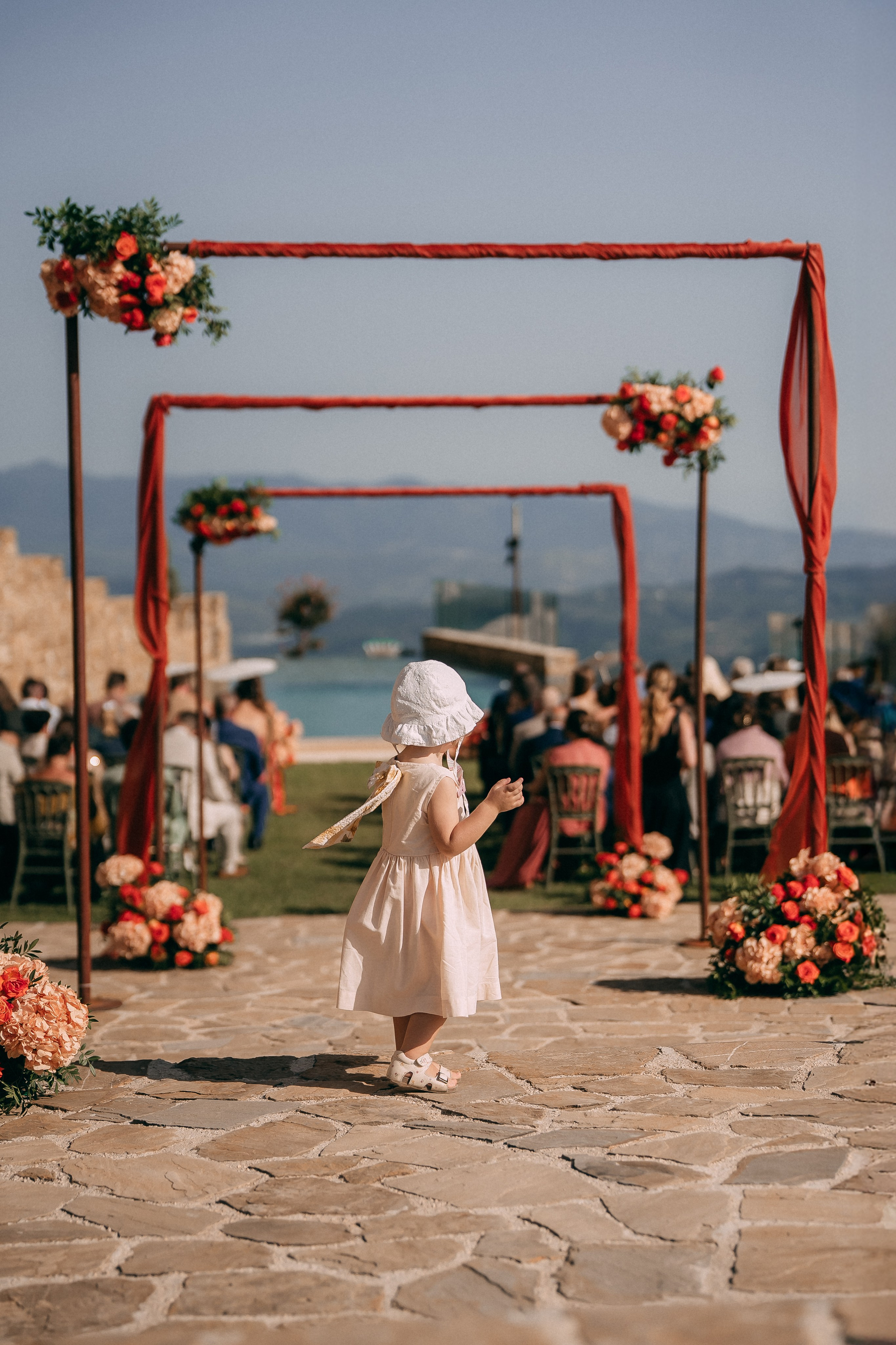 Flower girl walking down the aisle to the red floral ceremony arch