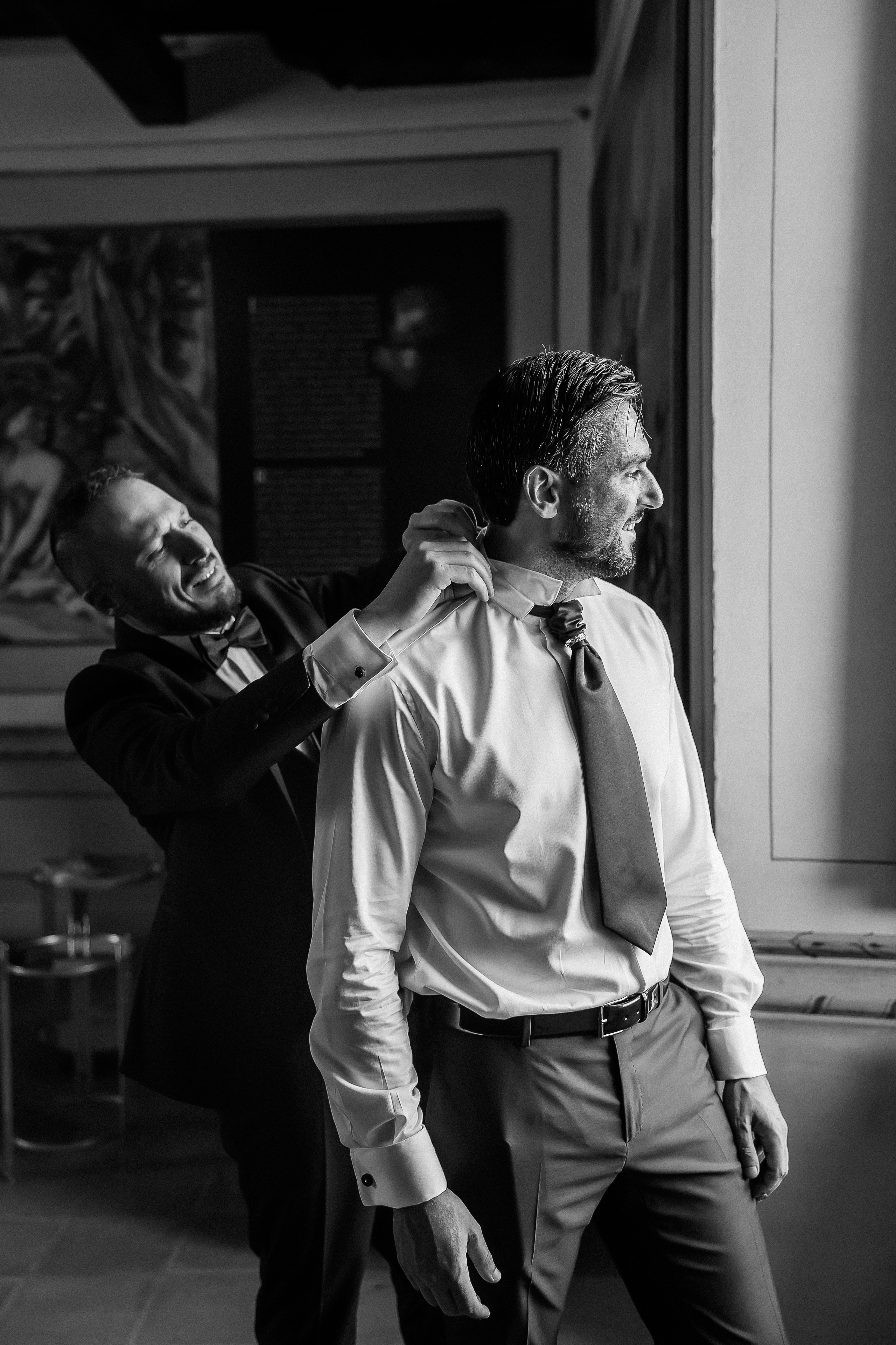 Black and white photo of the groom getting dressed with help from his best man