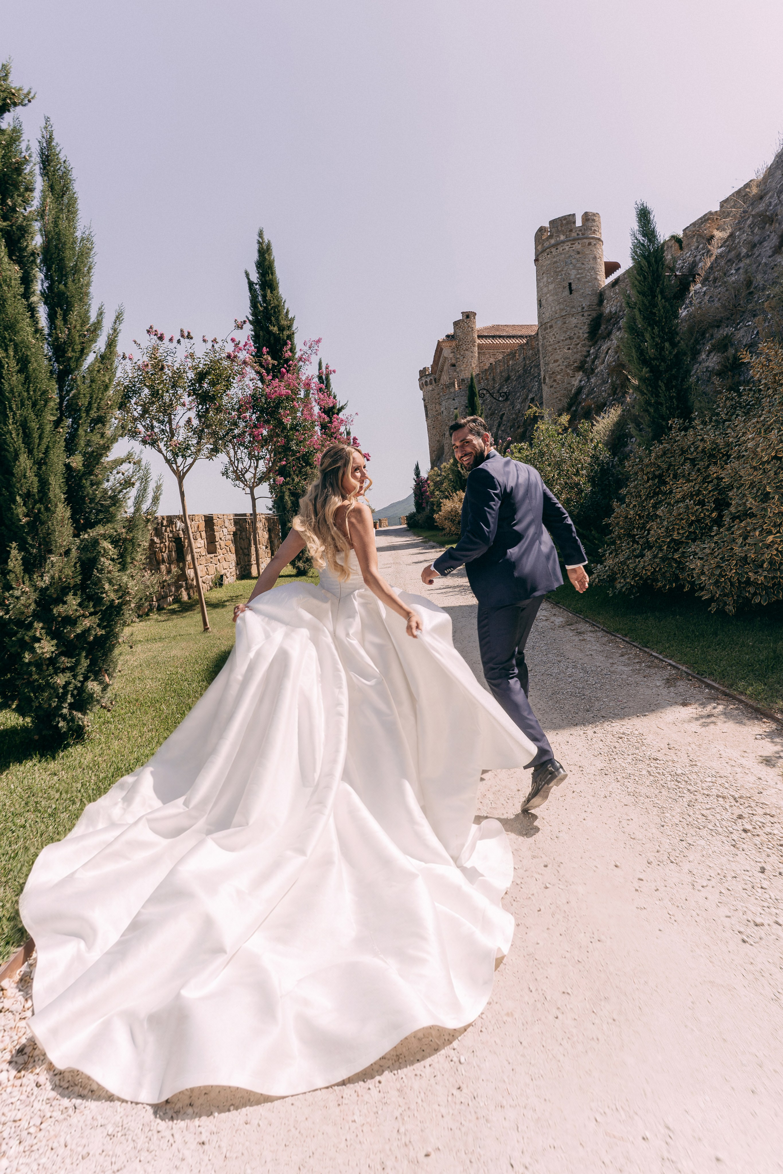 Bride running along the gravel path with the groom in the castle garden